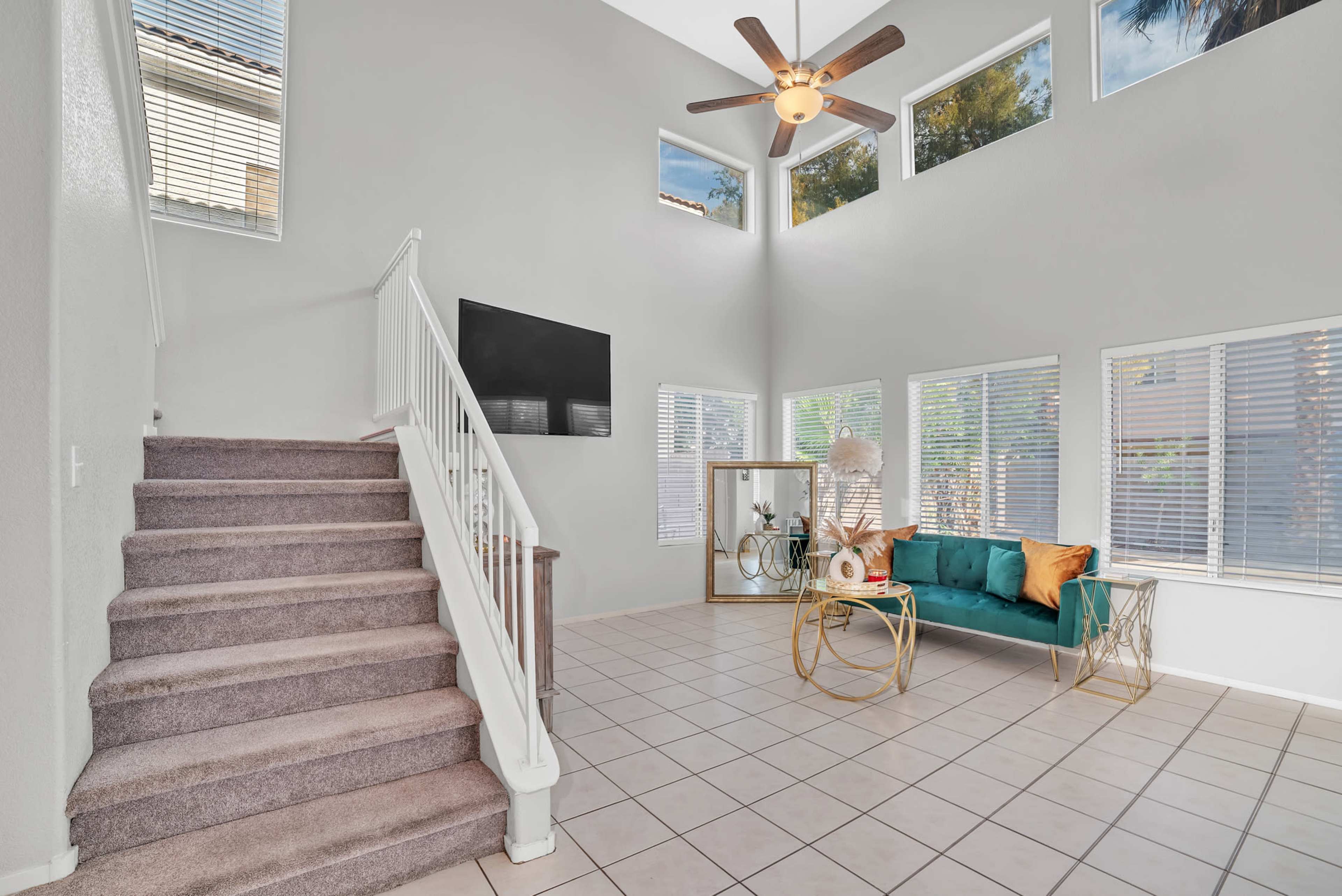 A spacious living area with a staircase, large windows, and a green sofa paired with decorative accents.
