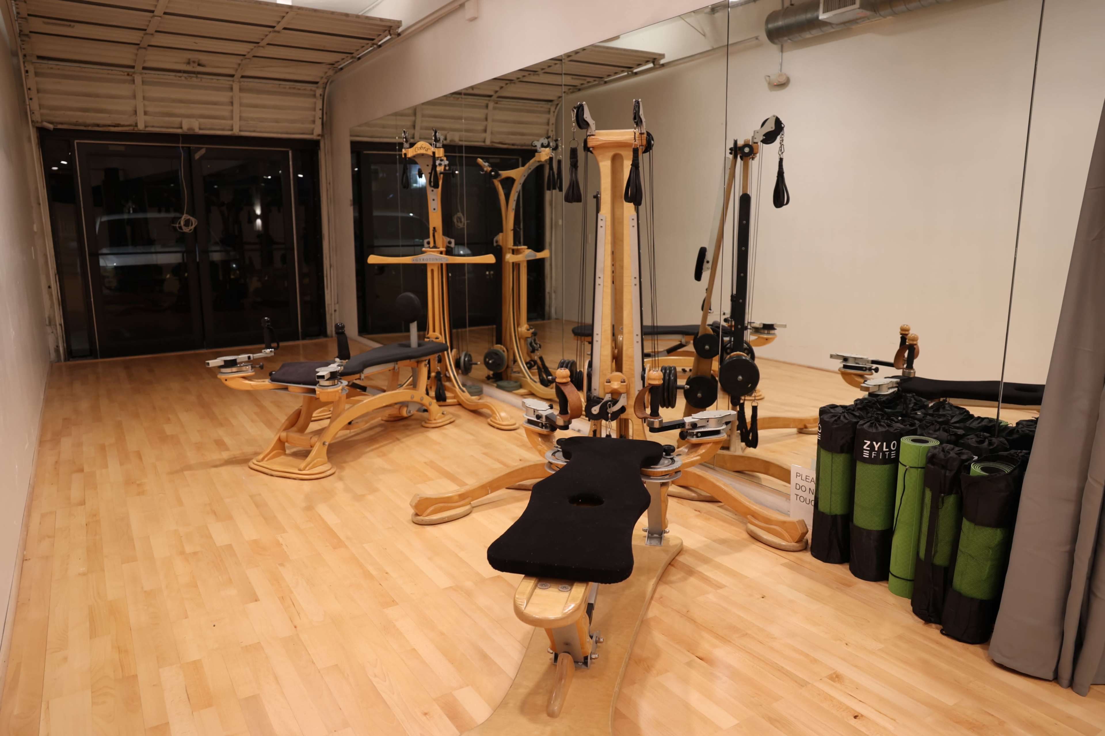 A spacious fitness studio with wooden exercise equipment, including reformer machines, and neatly arranged mats and accessories along the wall.