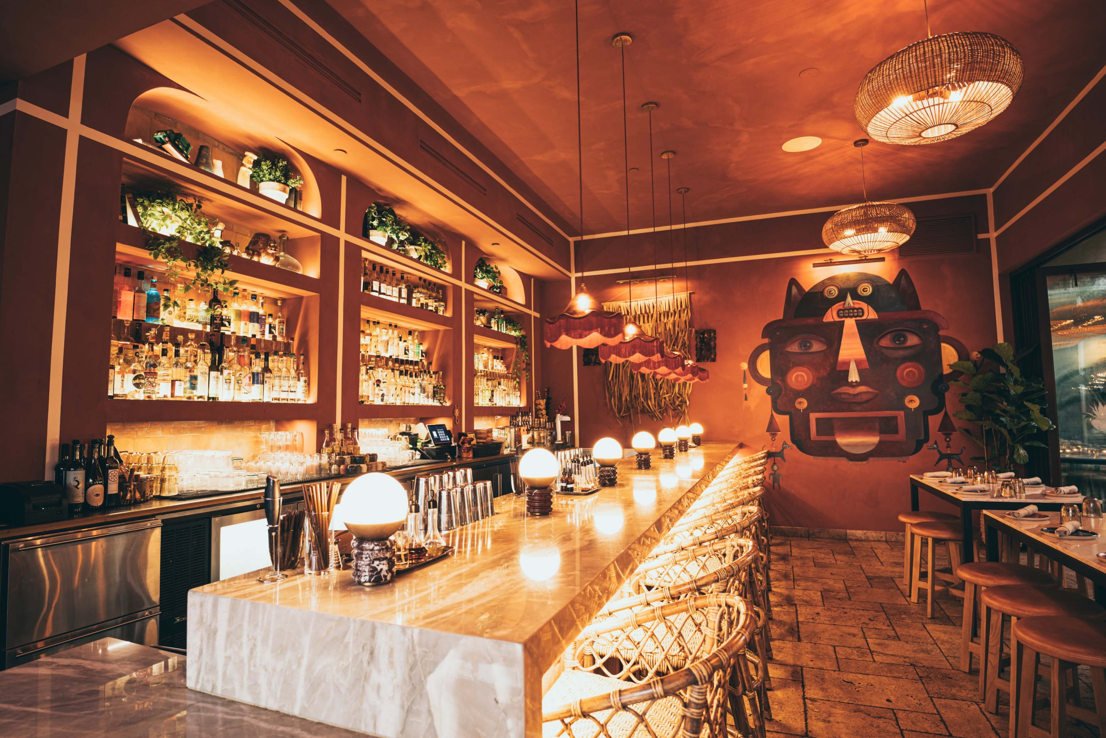 A stylish restaurant interior with a long marble bar, illuminated by round pendant lights and adorned with vibrant artwork on the walls.
