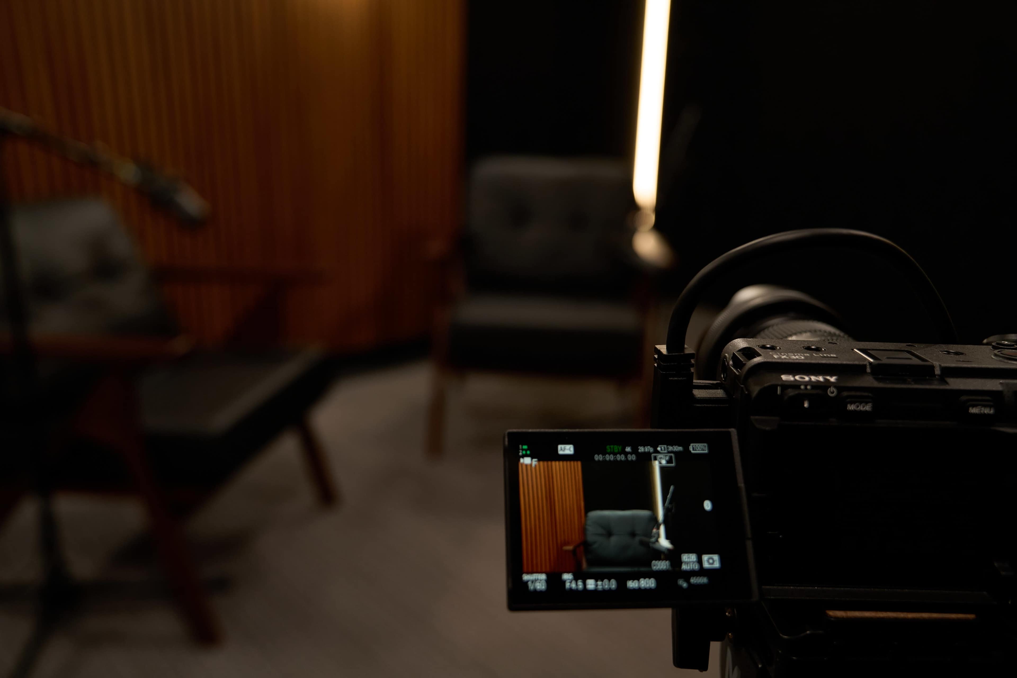 The image shows a camera focused on two empty chairs in a dimly lit interview setting.
