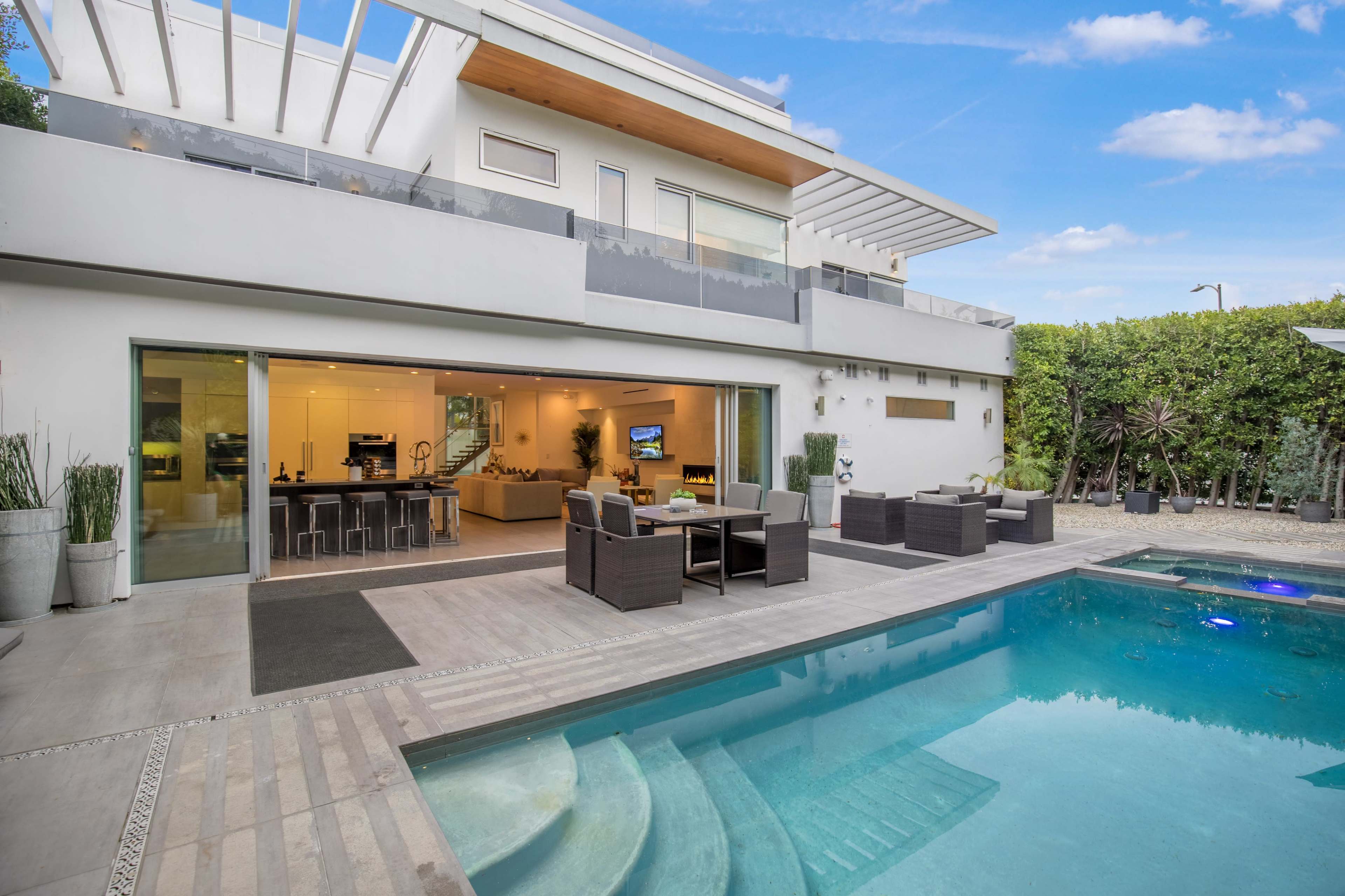 The image shows a modern home with a pool and outdoor seating area, featuring large glass doors that open to a spacious interior.