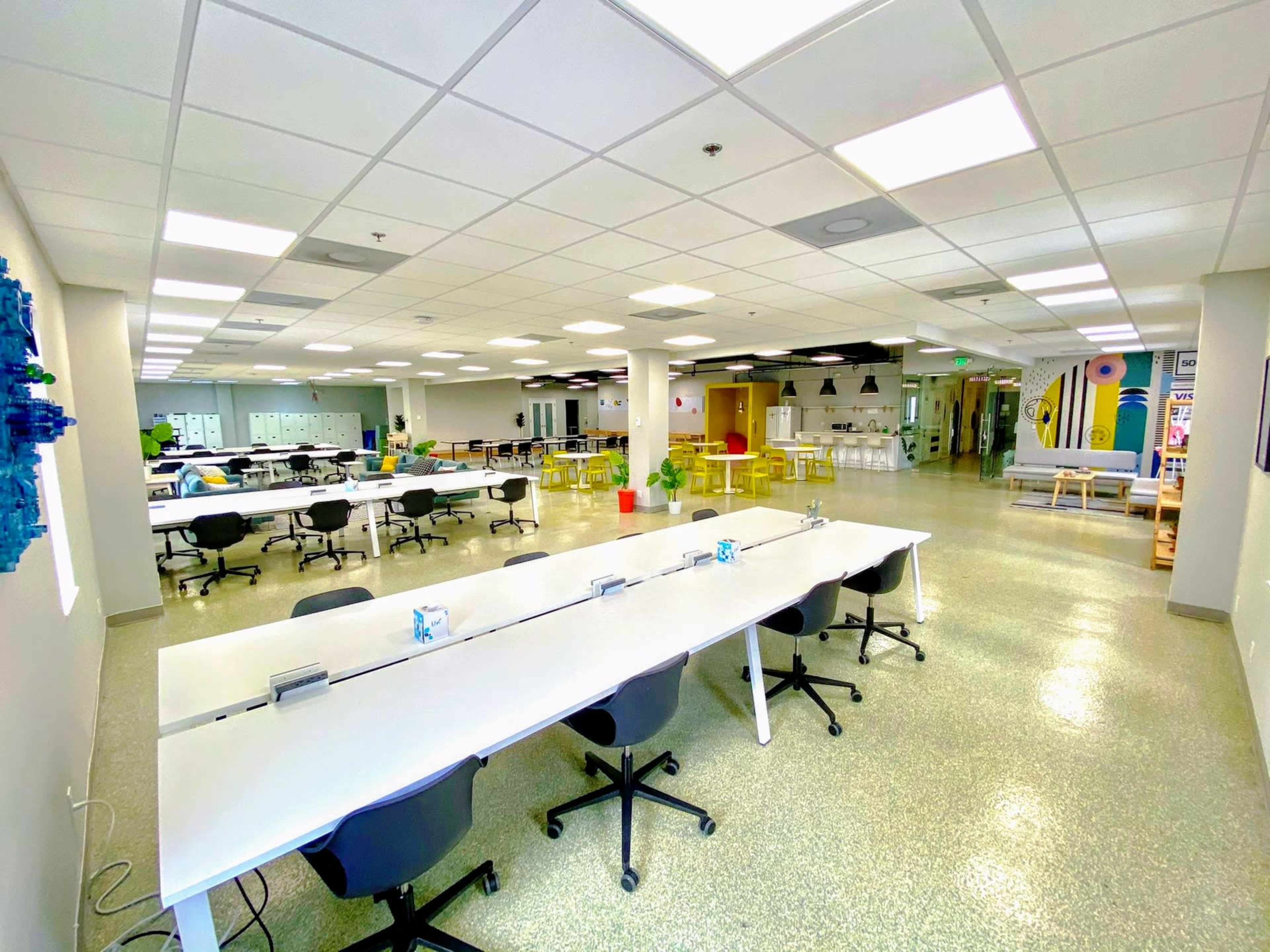 A spacious, well-lit office area with multiple long white tables and black chairs arranged in rows.
