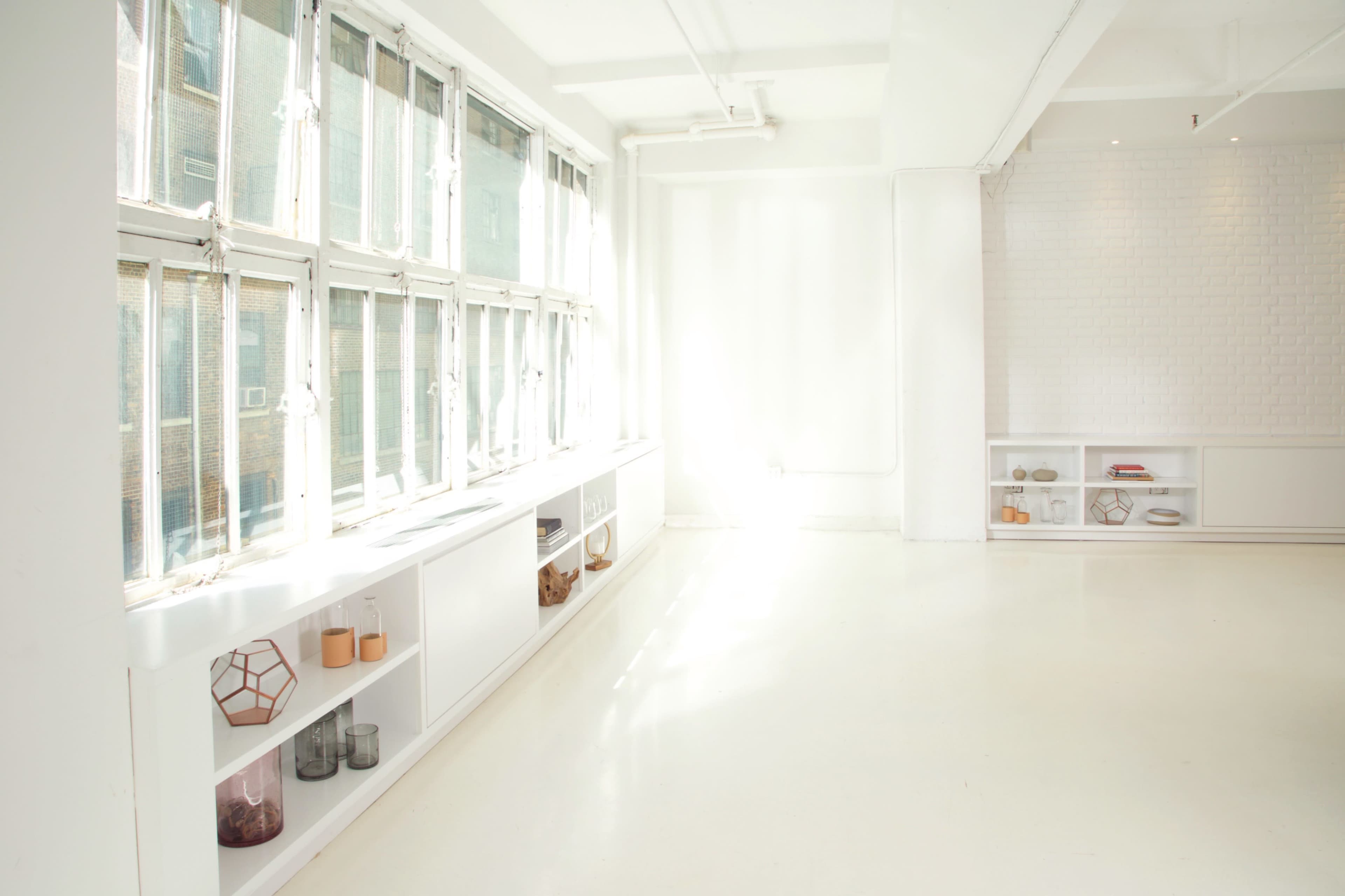 A bright, minimalistic room with large windows, white walls, and shelving units containing various decorative items.