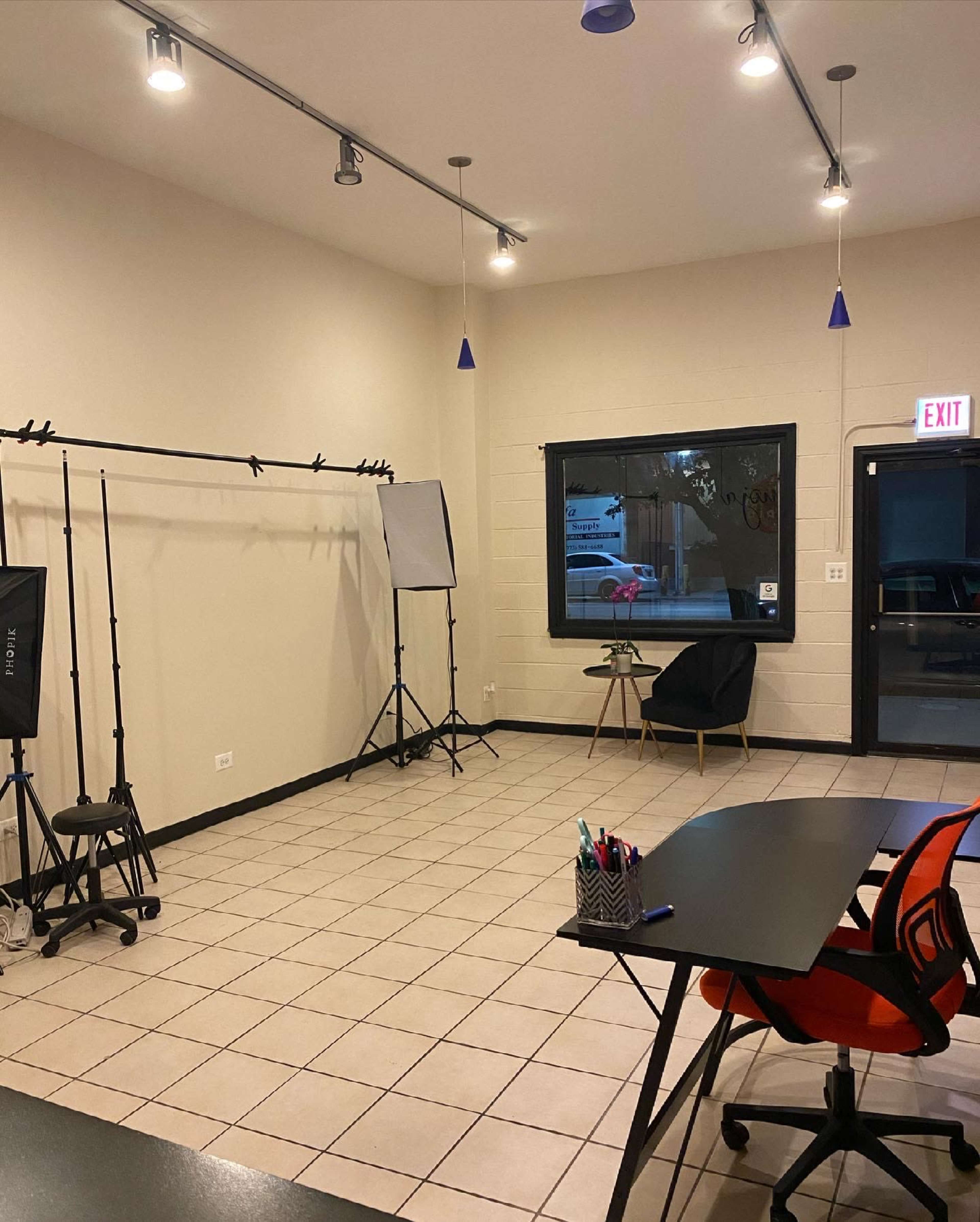 An empty studio space with a tiled floor, a desk and chairs, and studio lights set up against the walls.