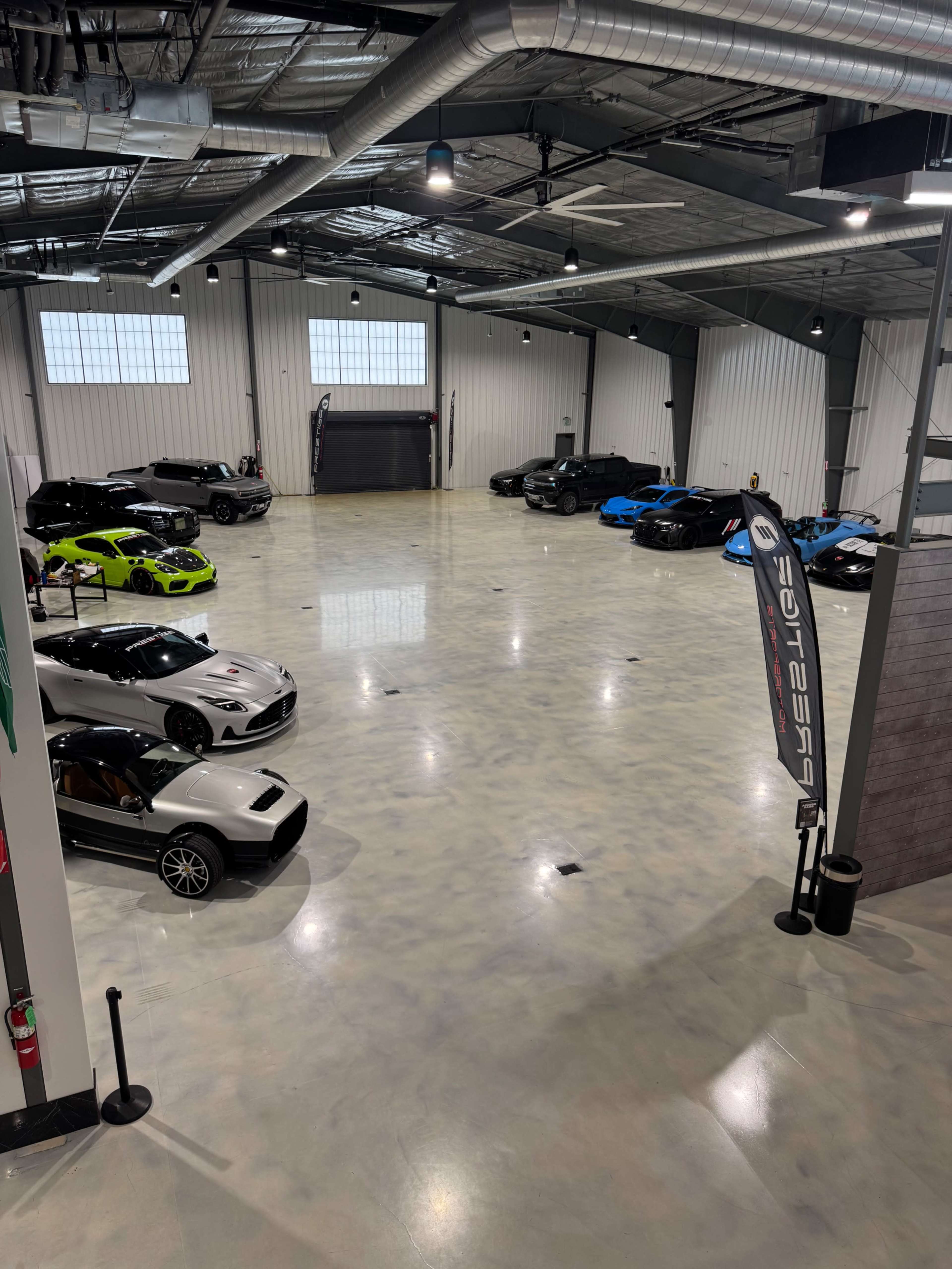The image shows a spacious garage or showroom with several luxury and sports cars displayed under bright overhead lights.
