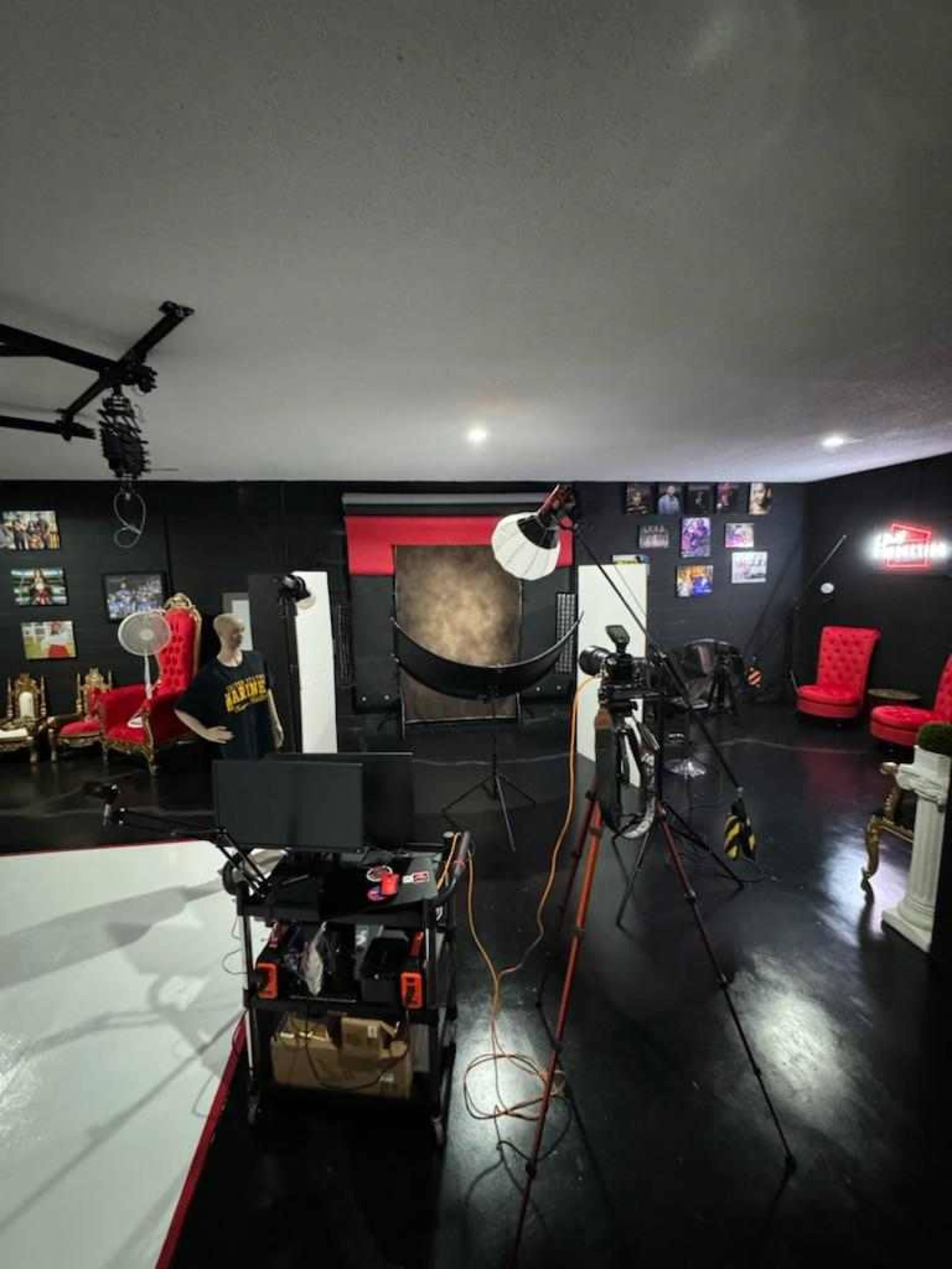 A photography studio features a backdrop, lighting equipment, and various props, along with red chairs and framed pictures on the walls.