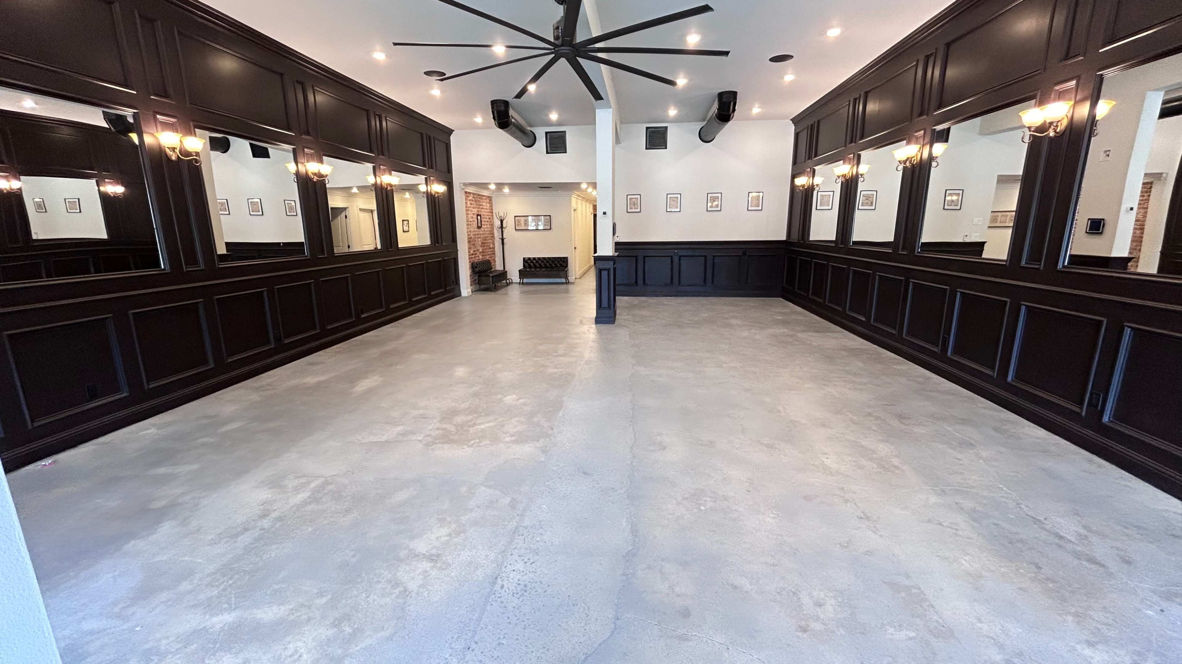 A spacious, empty room with dark wood paneling, large mirrors on the walls, and a polished concrete floor.