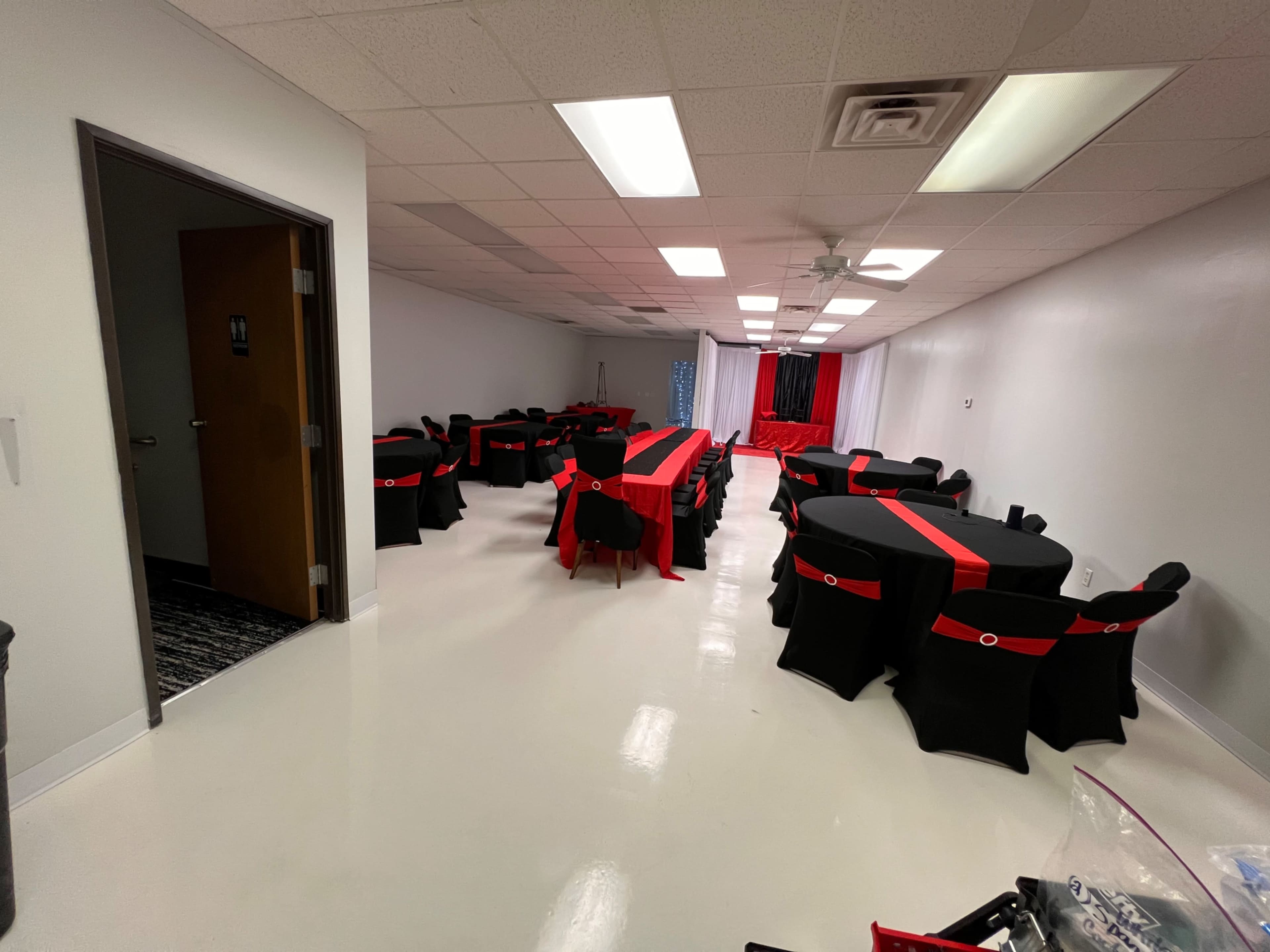 A banquet room with multiple black tables covered in red tablecloths, arranged in a symmetrical layout.