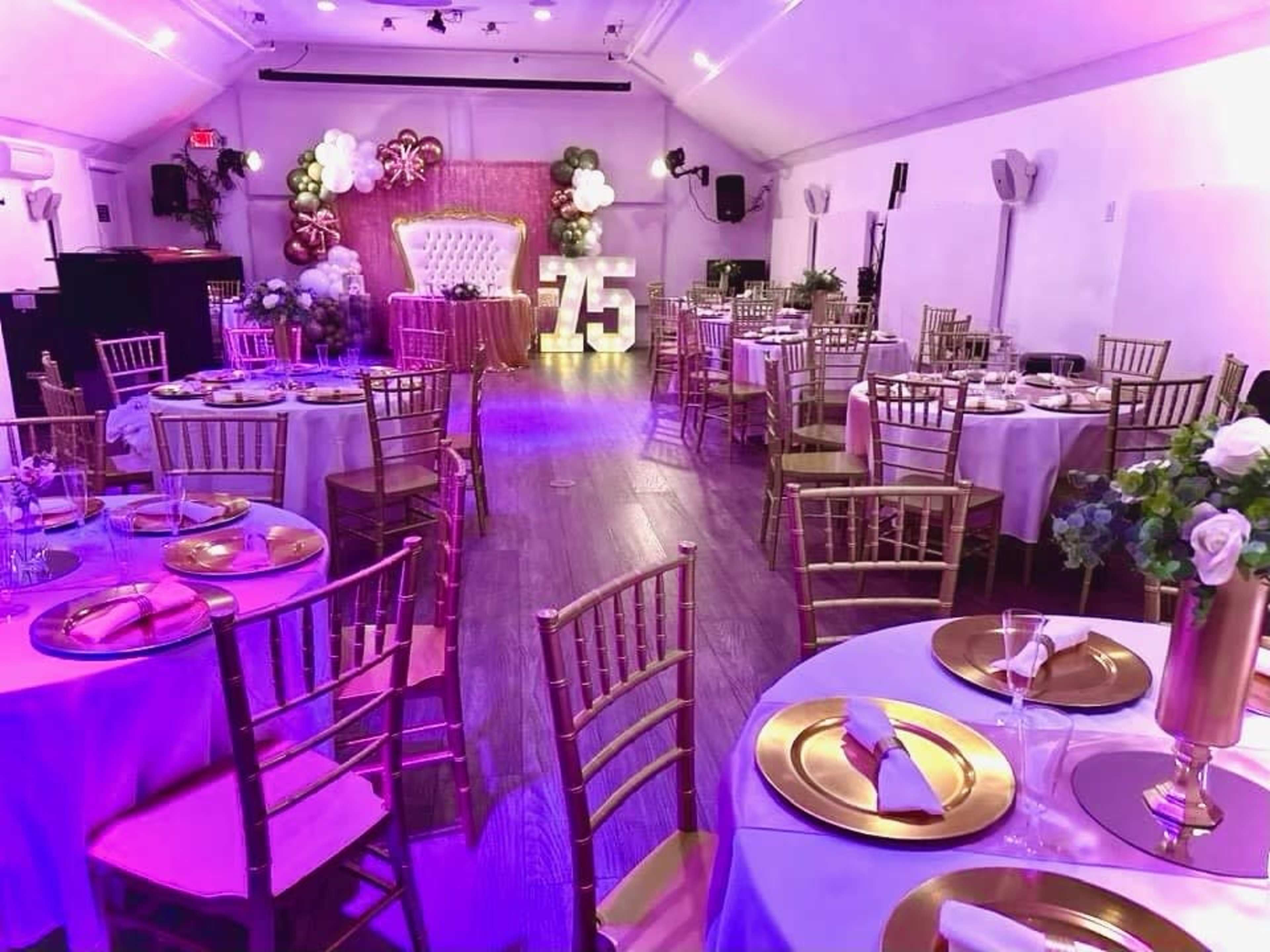 The image shows a decorated event space with tables set for a formal celebration, featuring gold accents, floral centerpieces, and a prominent "75" display in the background.