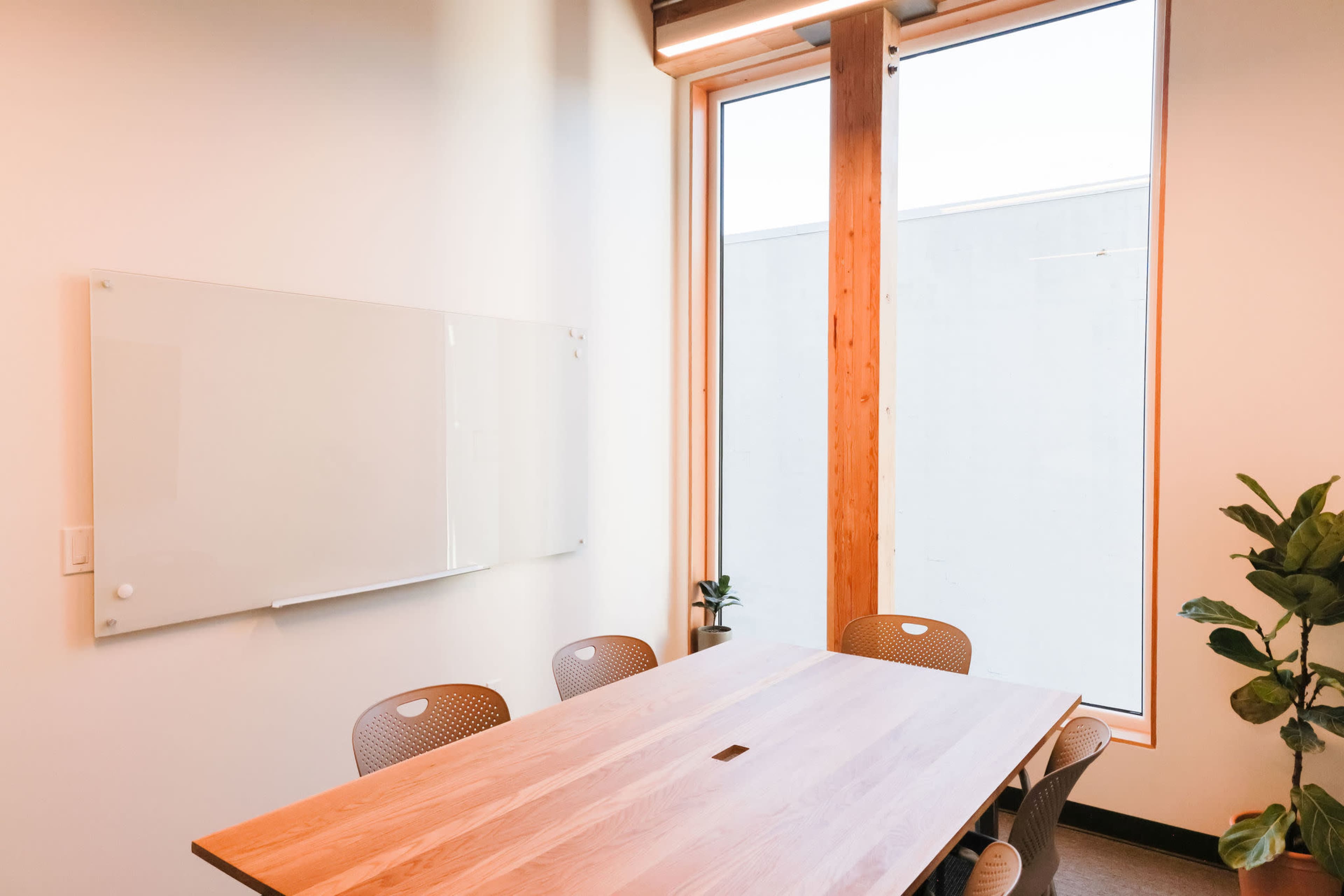A modern conference room with a wooden table, several chairs, a whiteboard on the wall, and large windows letting in natural light.