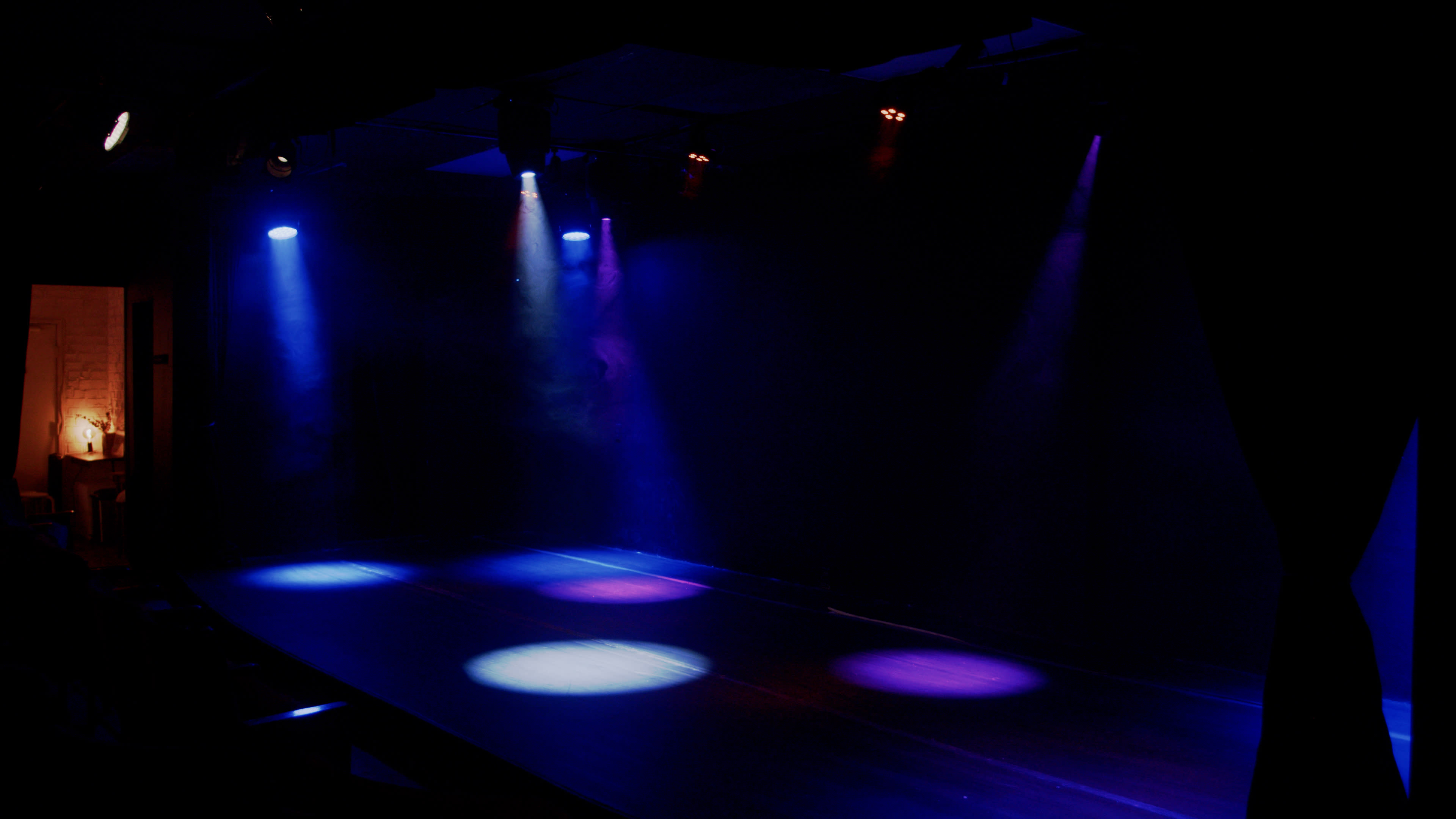 A dimly lit stage with circular spots of colored light and a backdrop of dark walls.