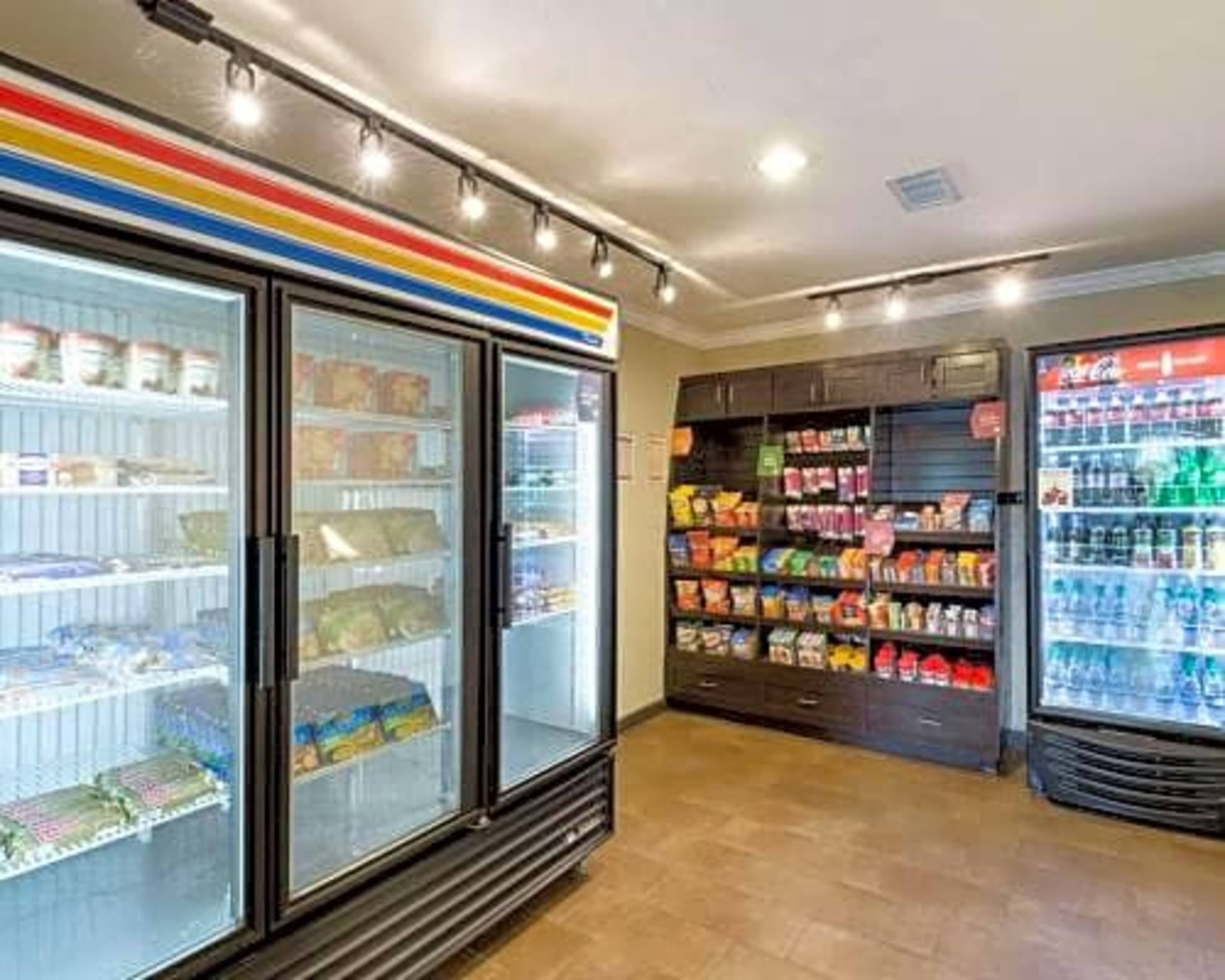 A convenience store interior with two refrigerators displaying frozen goods and a shelving unit filled with snacks and beverages.