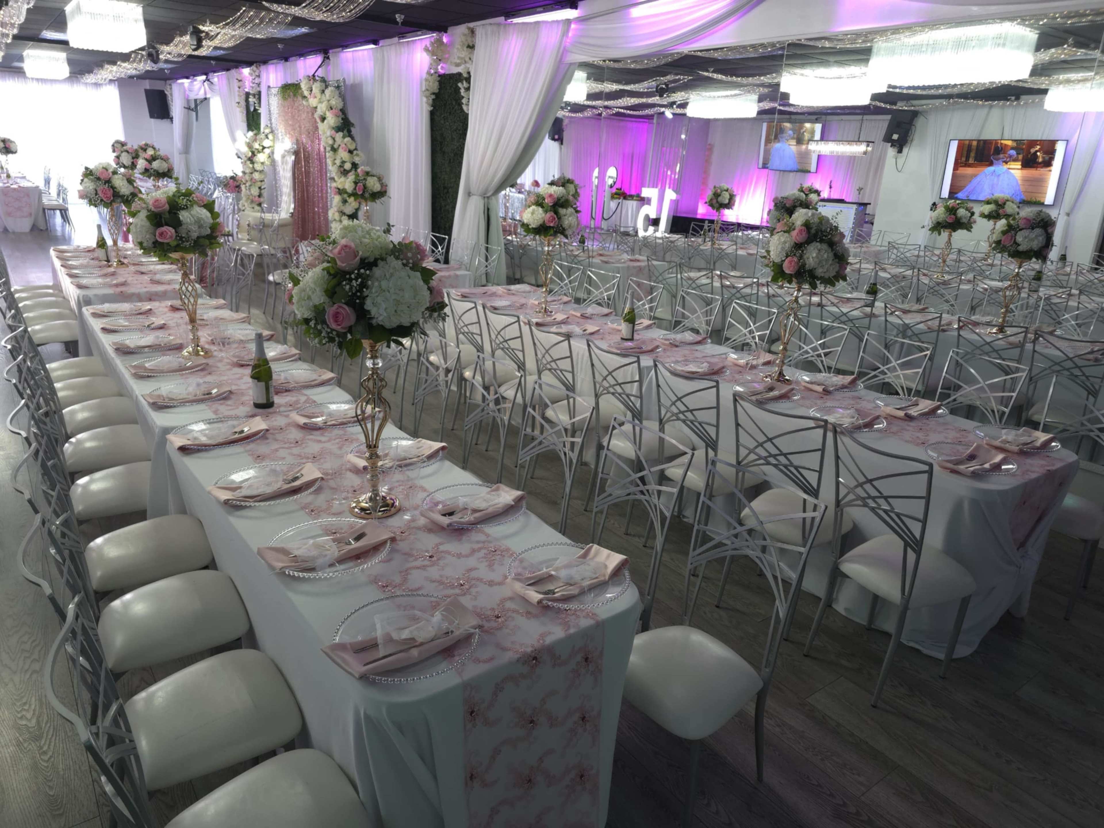 The image shows a elegantly arranged banquet hall with long tables set for an event, adorned with floral centerpieces and draped fabrics.