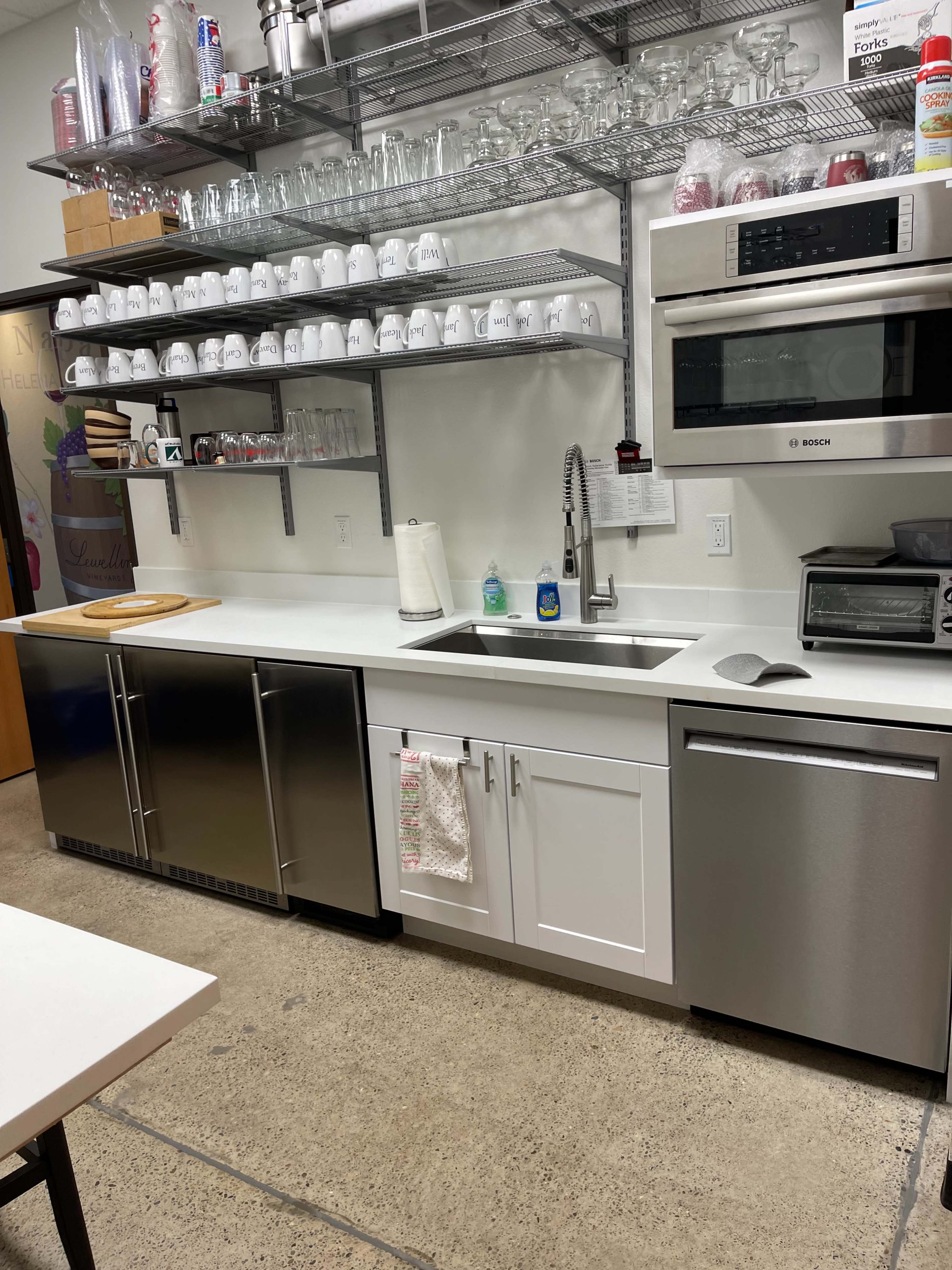 A modern kitchen with stainless steel appliances, white cabinets, a large sink, and shelves holding glasses and dishes.