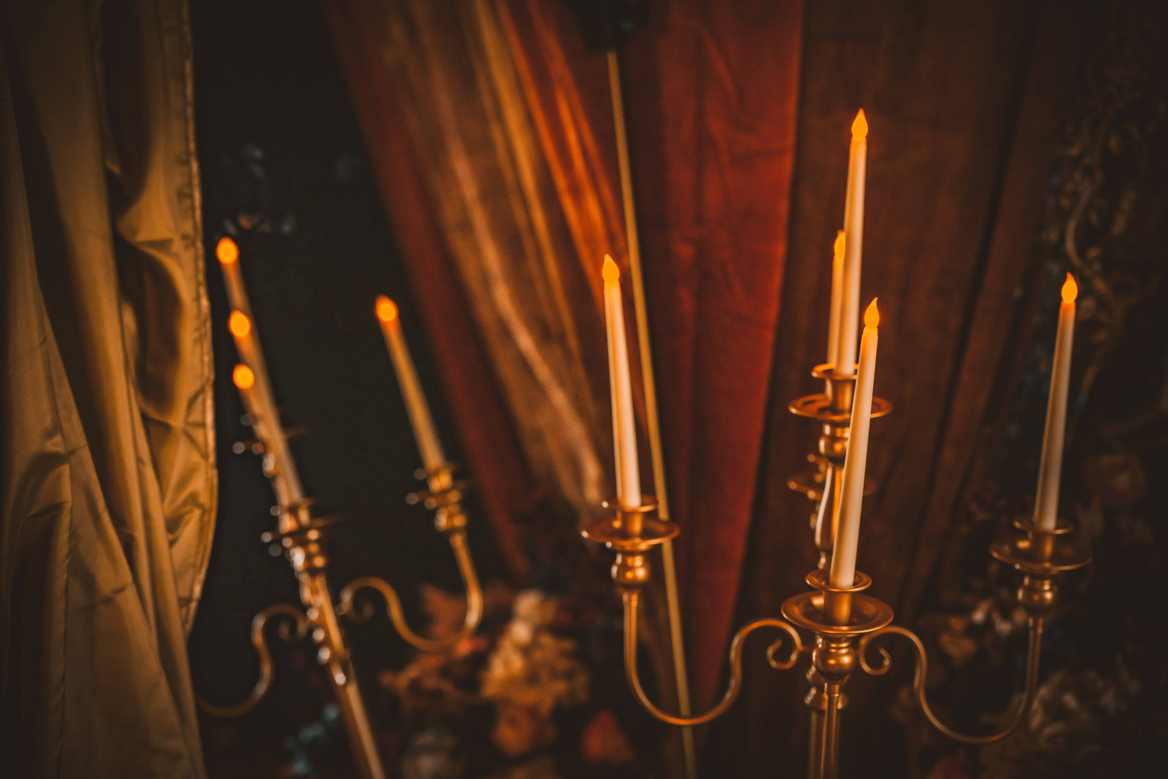 Several gold candlesticks with lit white candles arranged against a dark backdrop.