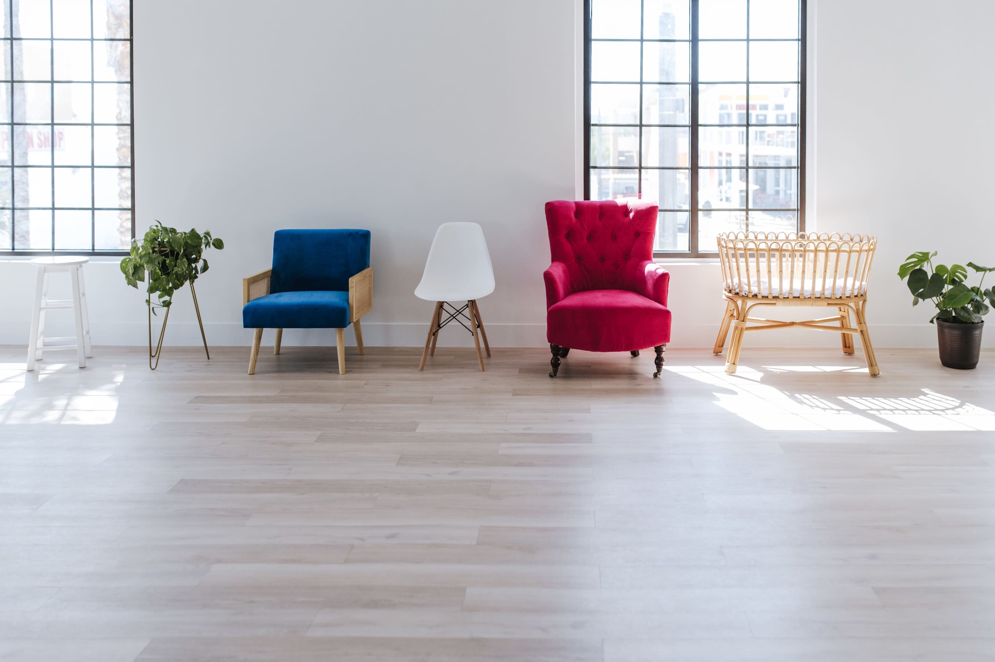 A bright and spacious room featuring four distinct chairs and two potted plants positioned near large windows.
