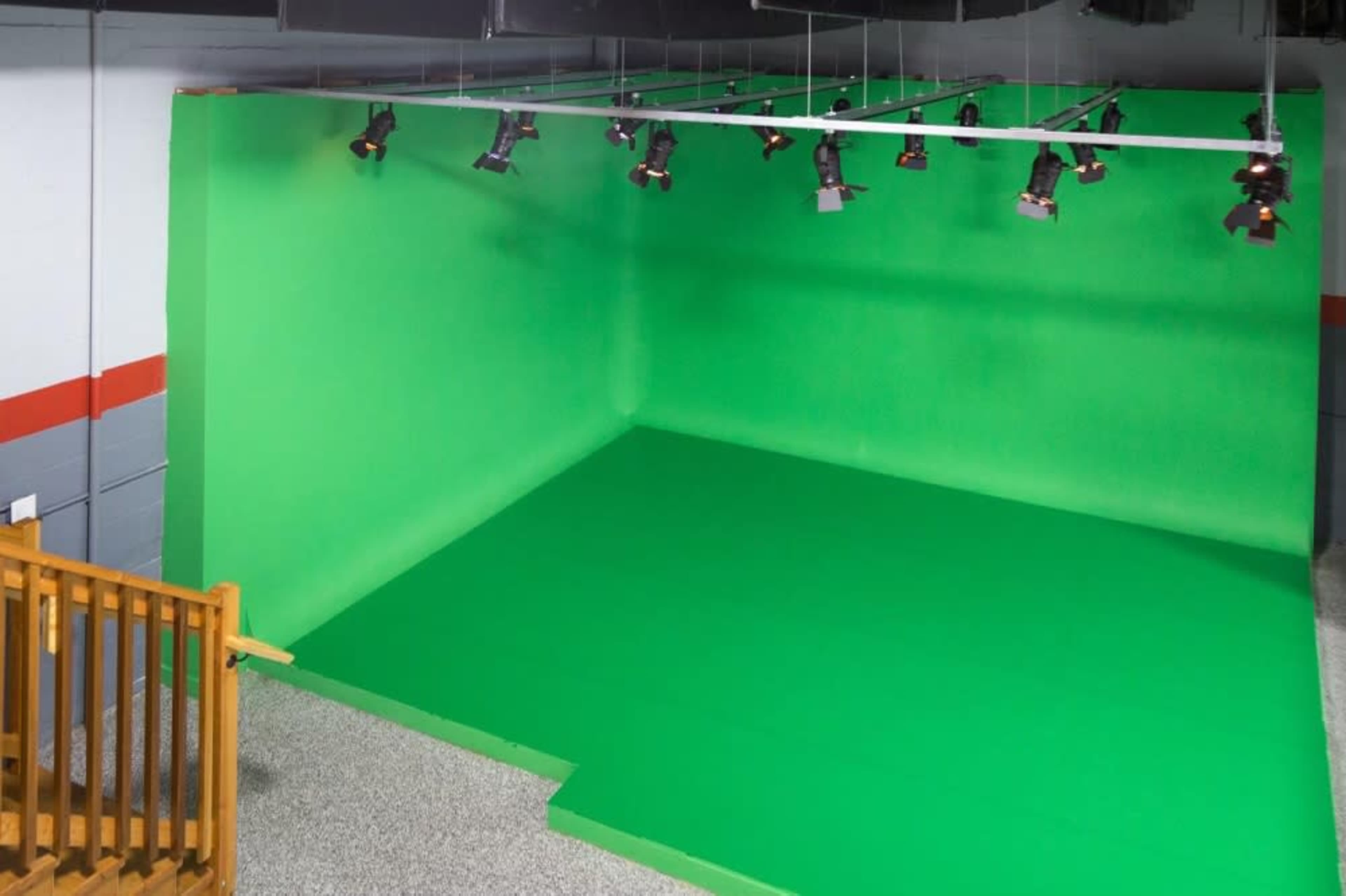 A large green screen studio with overhead lights and a smooth green floor.