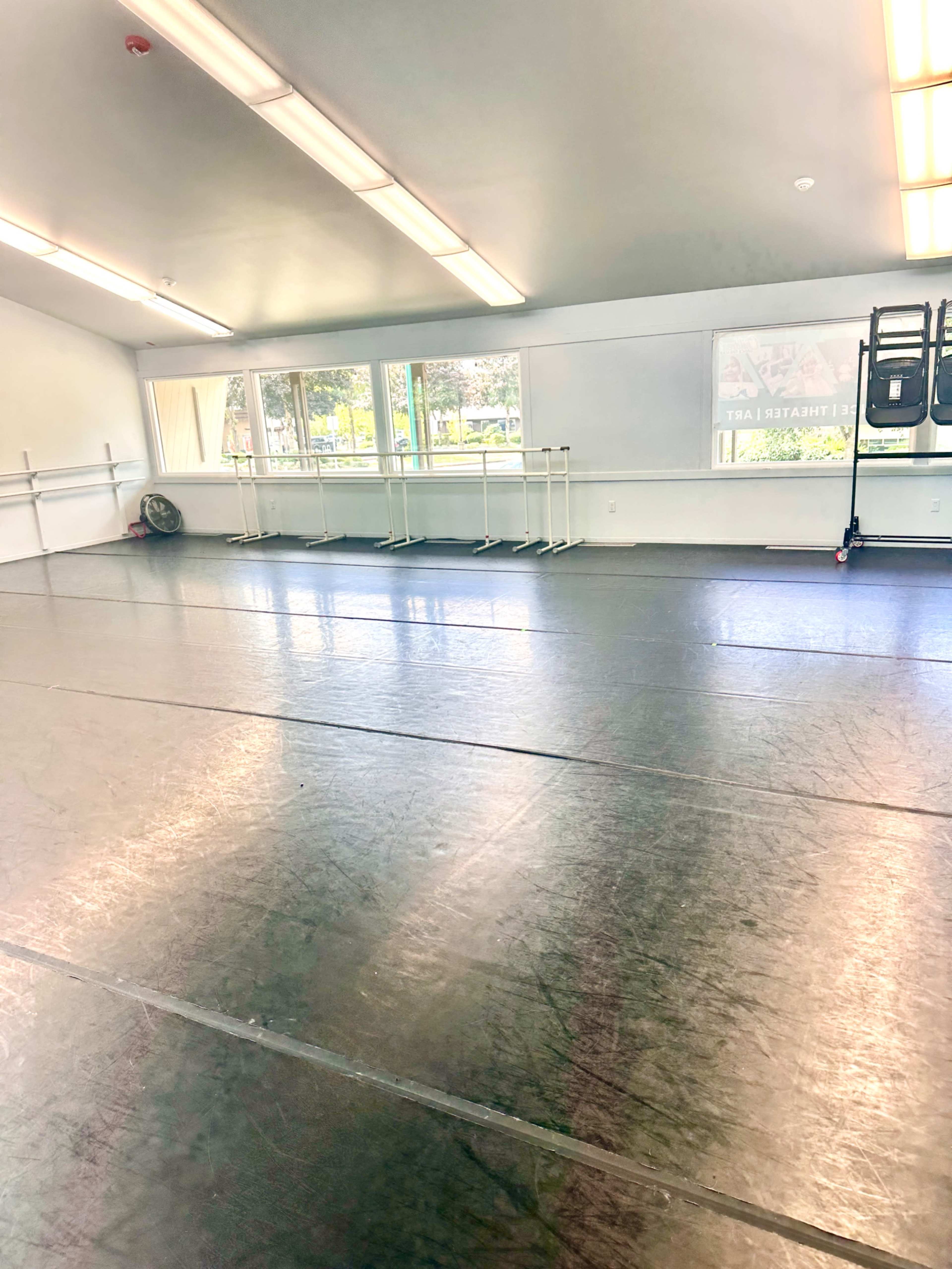 The image depicts an empty dance studio with mirrors along one wall and several ballet barres.