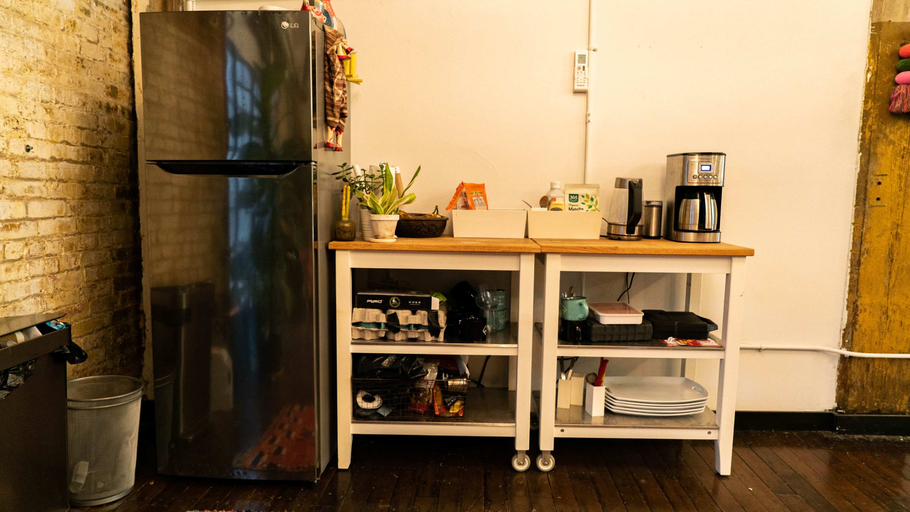 A kitchen space with a stainless steel refrigerator, a countertop with a coffee maker, and shelves holding various kitchen items and utensils.