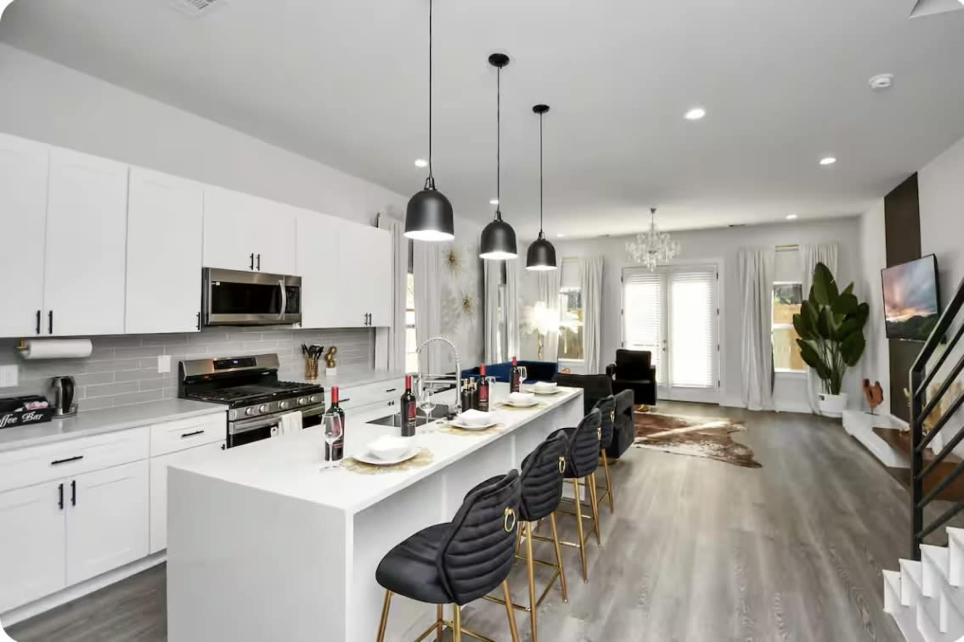 The modern kitchen features white cabinetry, a large island with seating, and sleek black pendant lights, complemented by stainless steel appliances and an open layout.