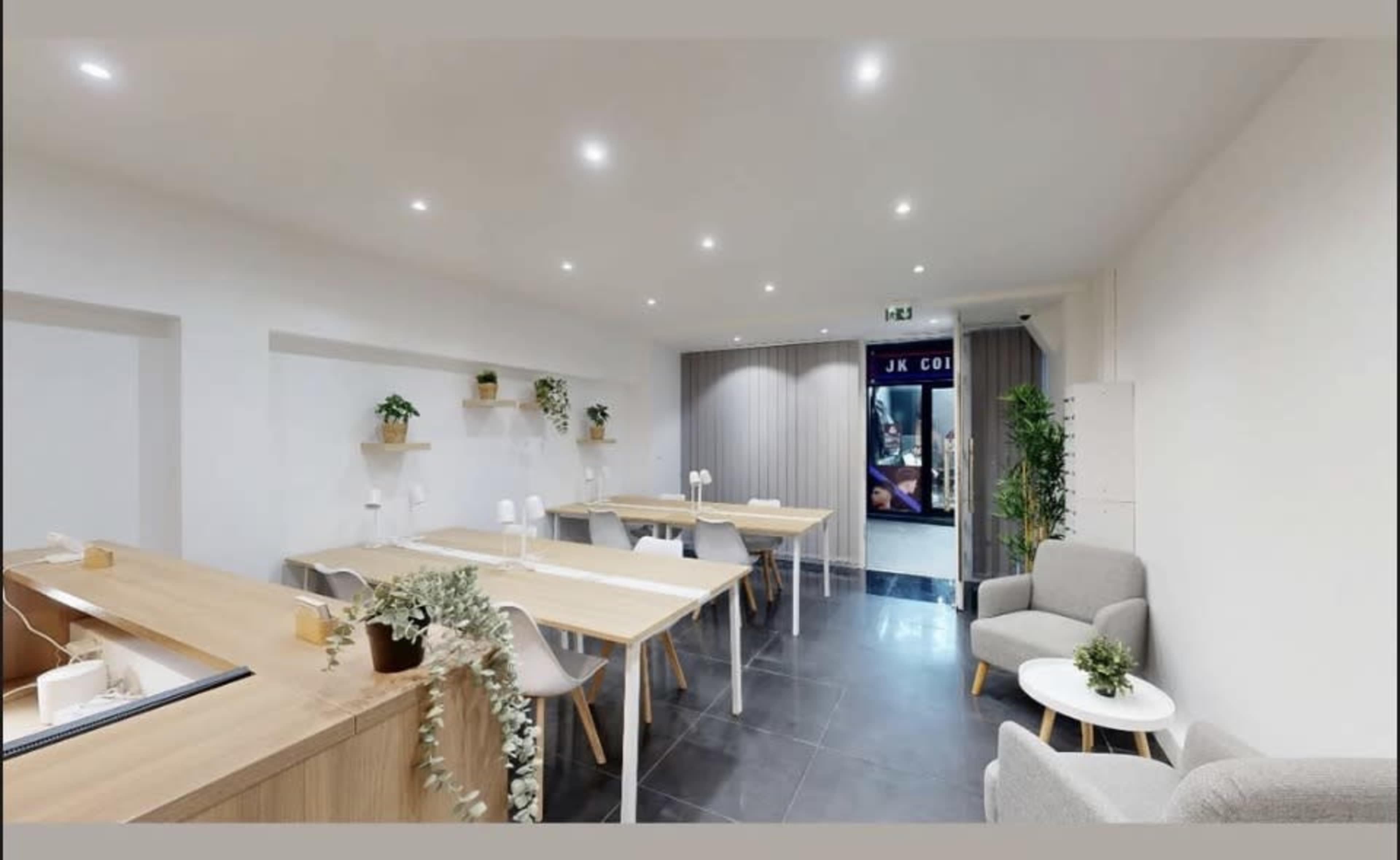 The image shows a modern, minimalist interior of a café with wooden tables, potted plants, and a seating area beside a glass door.