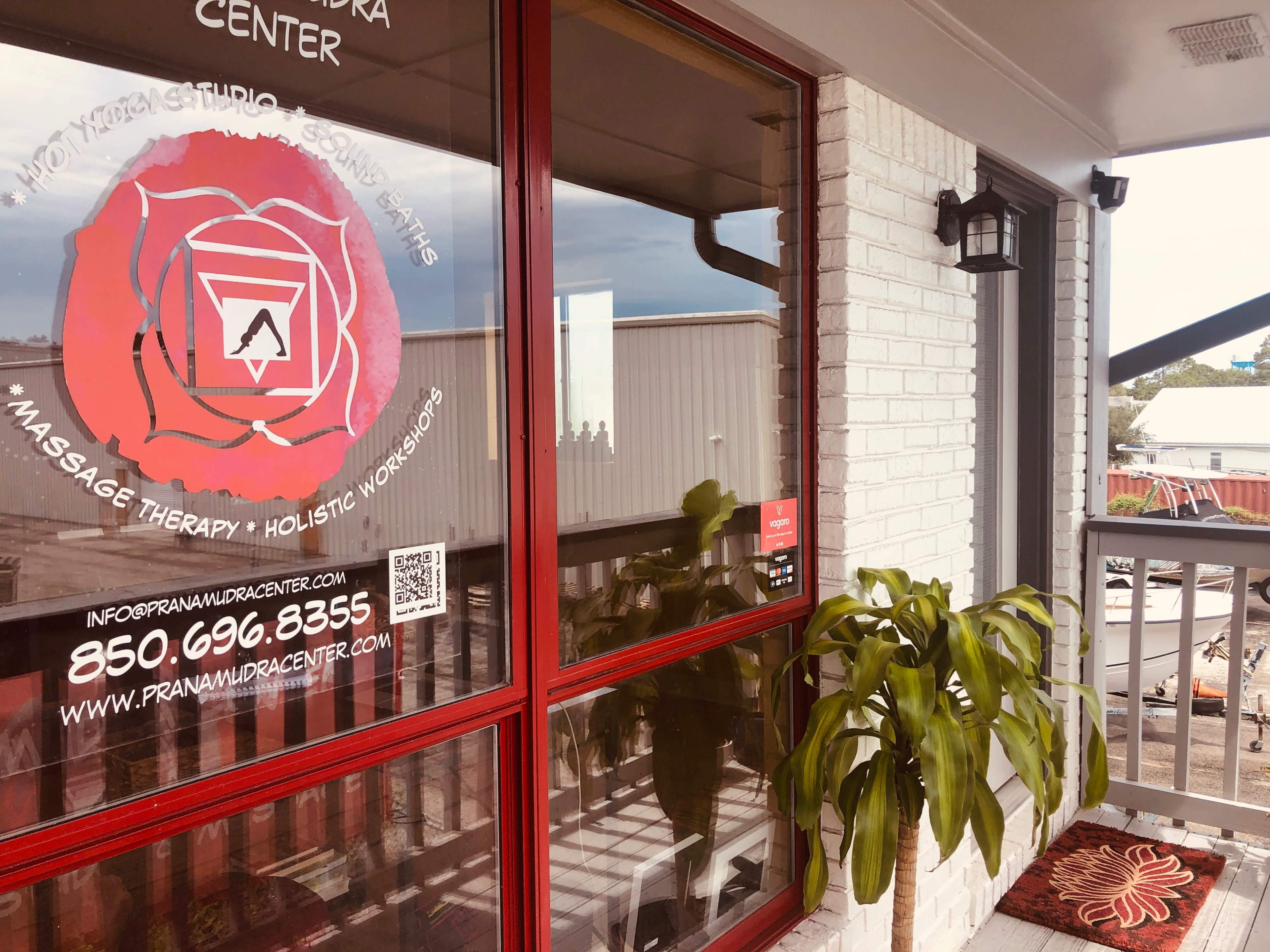 The image shows a balcony area featuring a potted plant and a window with signage for a massage therapy and holistic workshops center.
