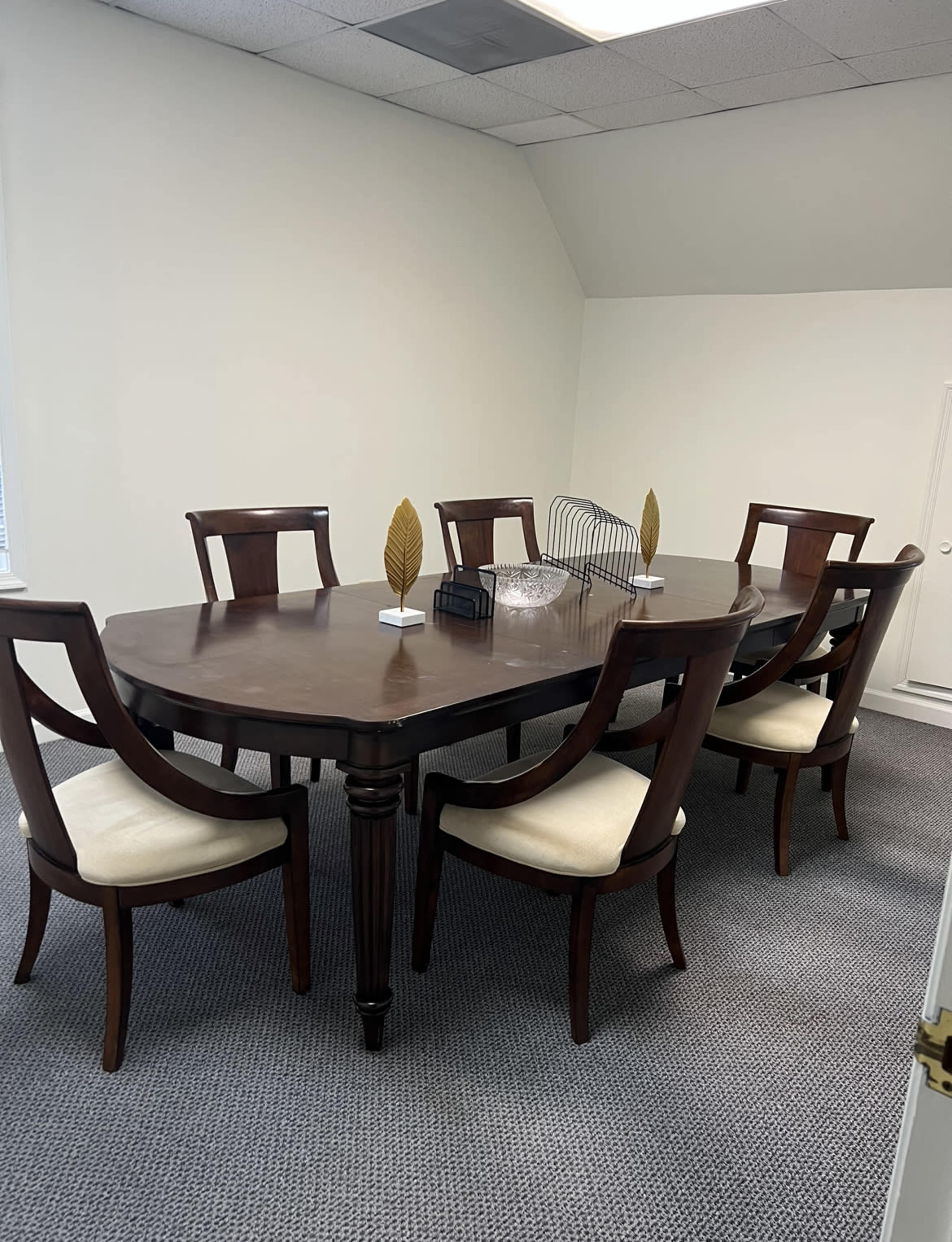 A wooden conference table surrounded by six upholstered chairs is set in a well-lit room.