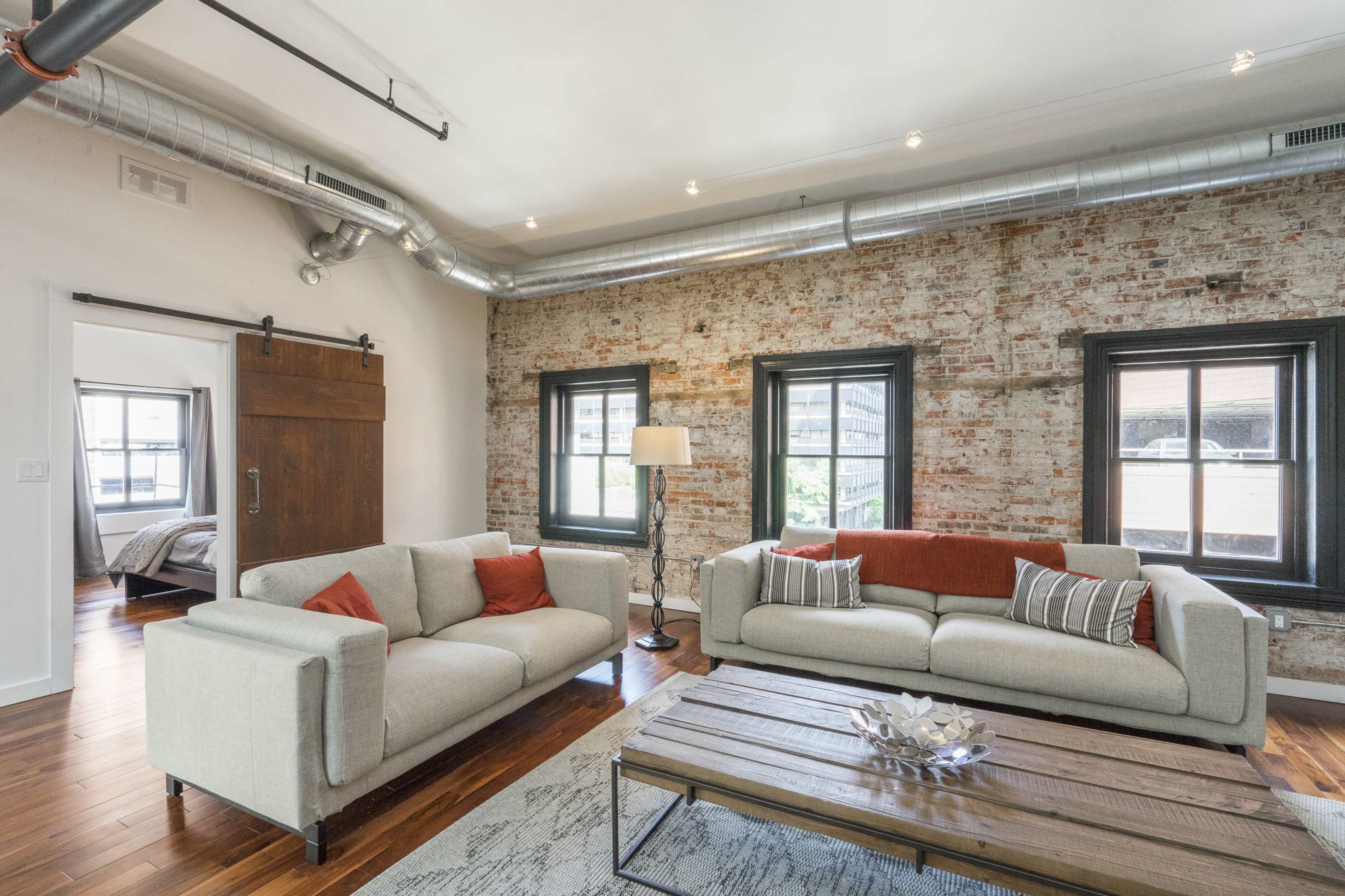 A modern living room with exposed brick walls, large windows, and a wooden coffee table between two sofas.
