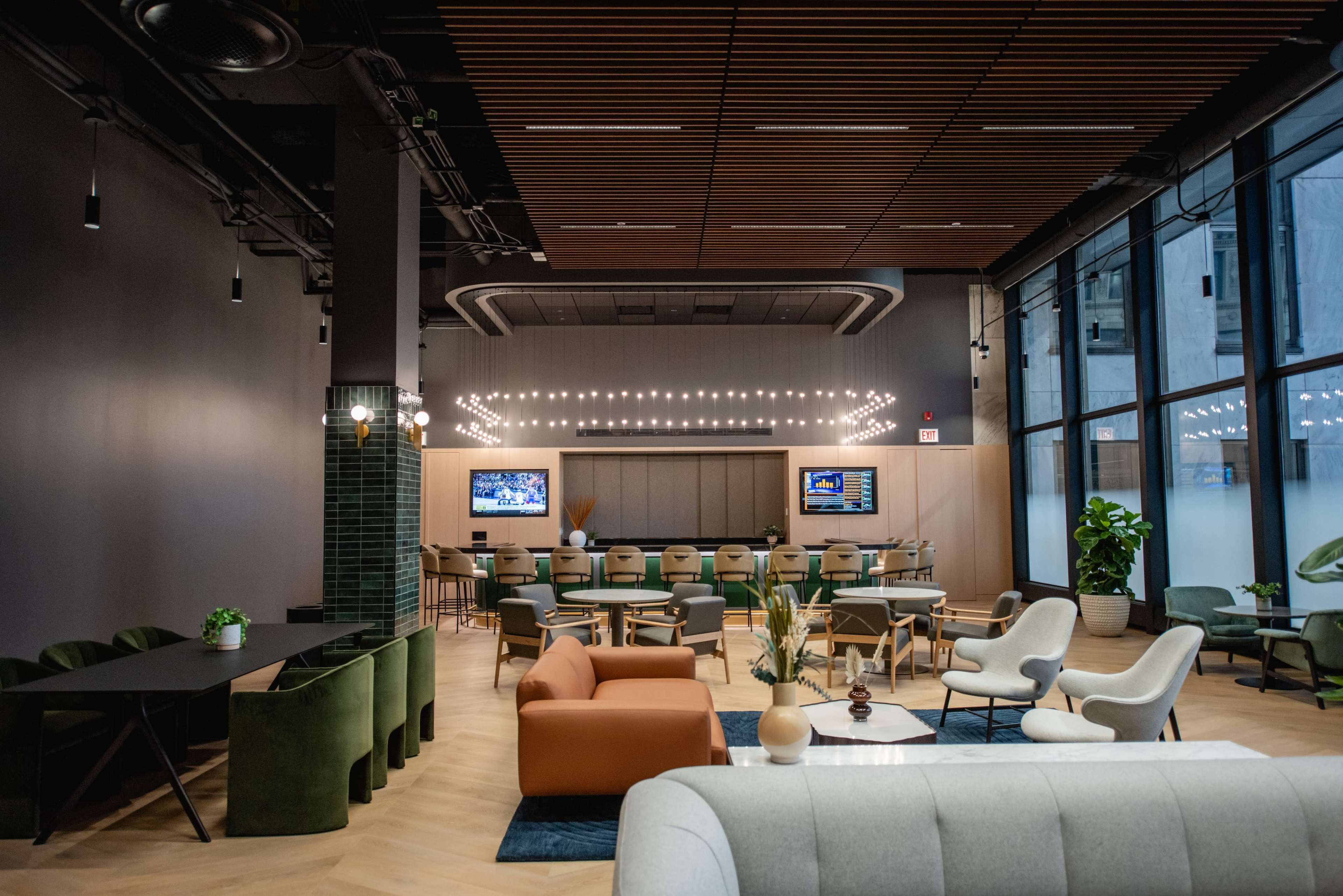 The scene features a modern, open-plan lounge area with a mix of seating arrangements, including chairs, sofas, and tables, illuminated by warm overhead lights.