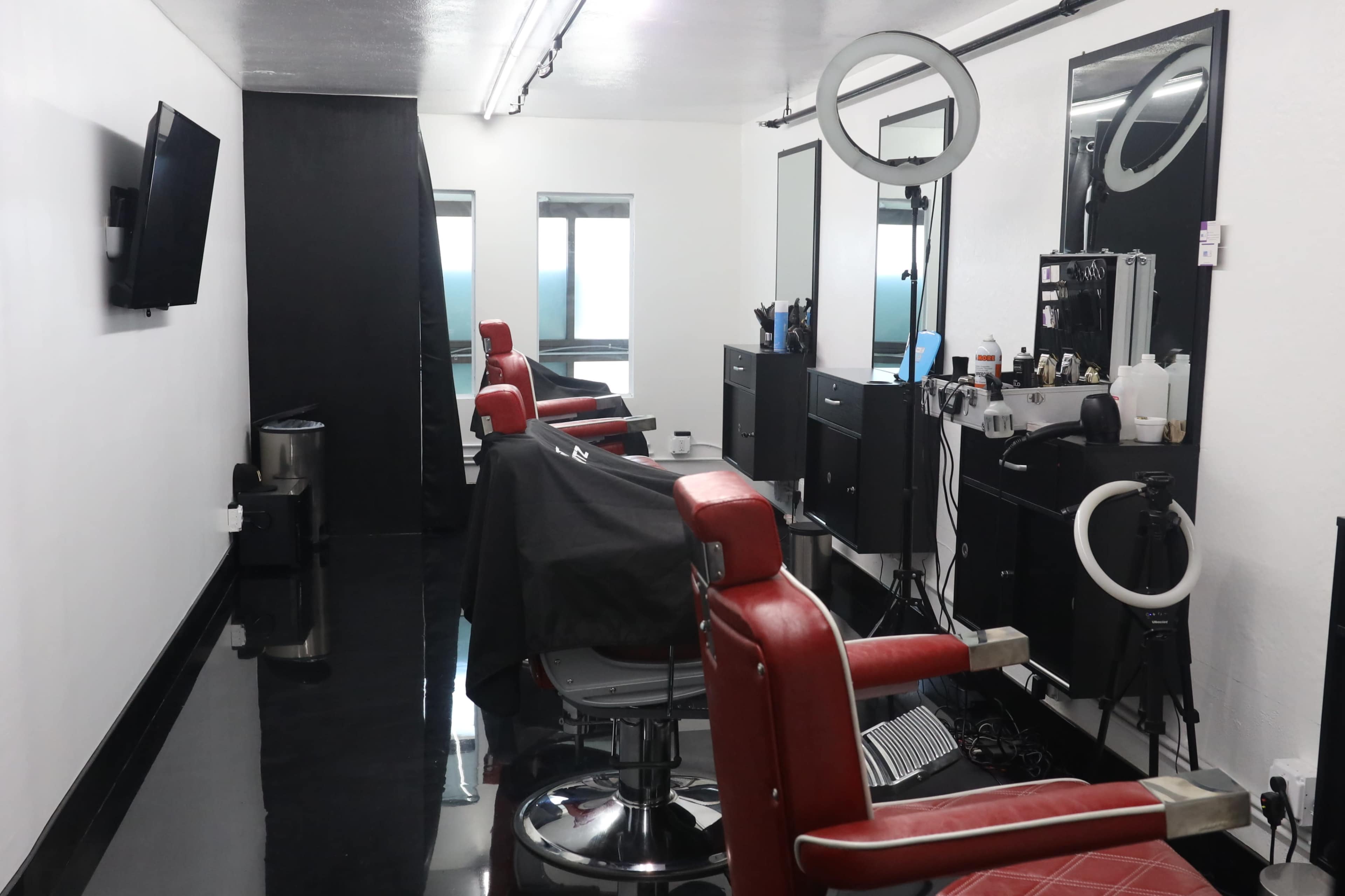 The interior of a barbershop features red leather chairs, mirrors, and a black floor, with a setup for grooming tools and equipment.