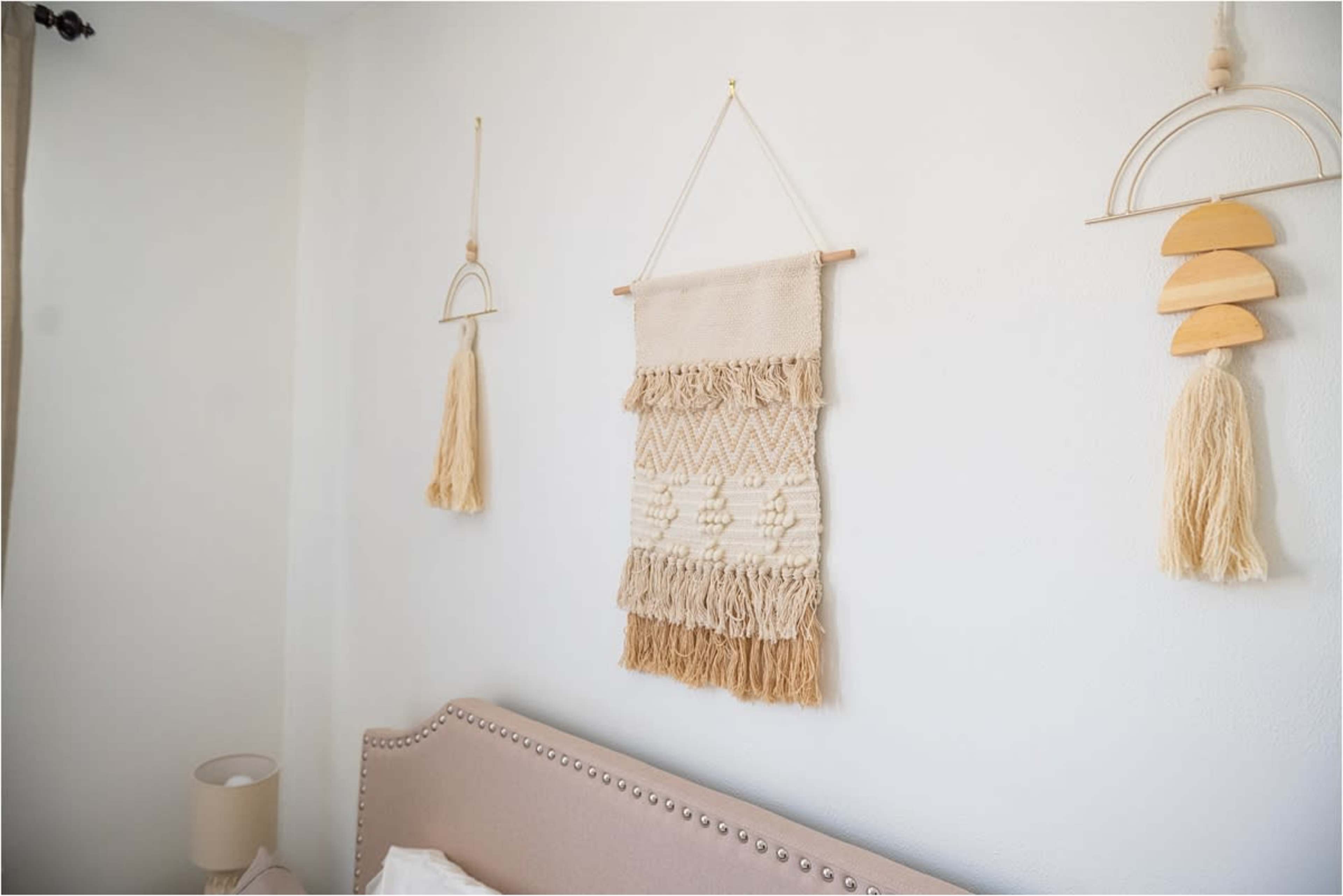 A light-colored bedroom wall adorned with a woven wall hanging and two decorative wooden pieces.