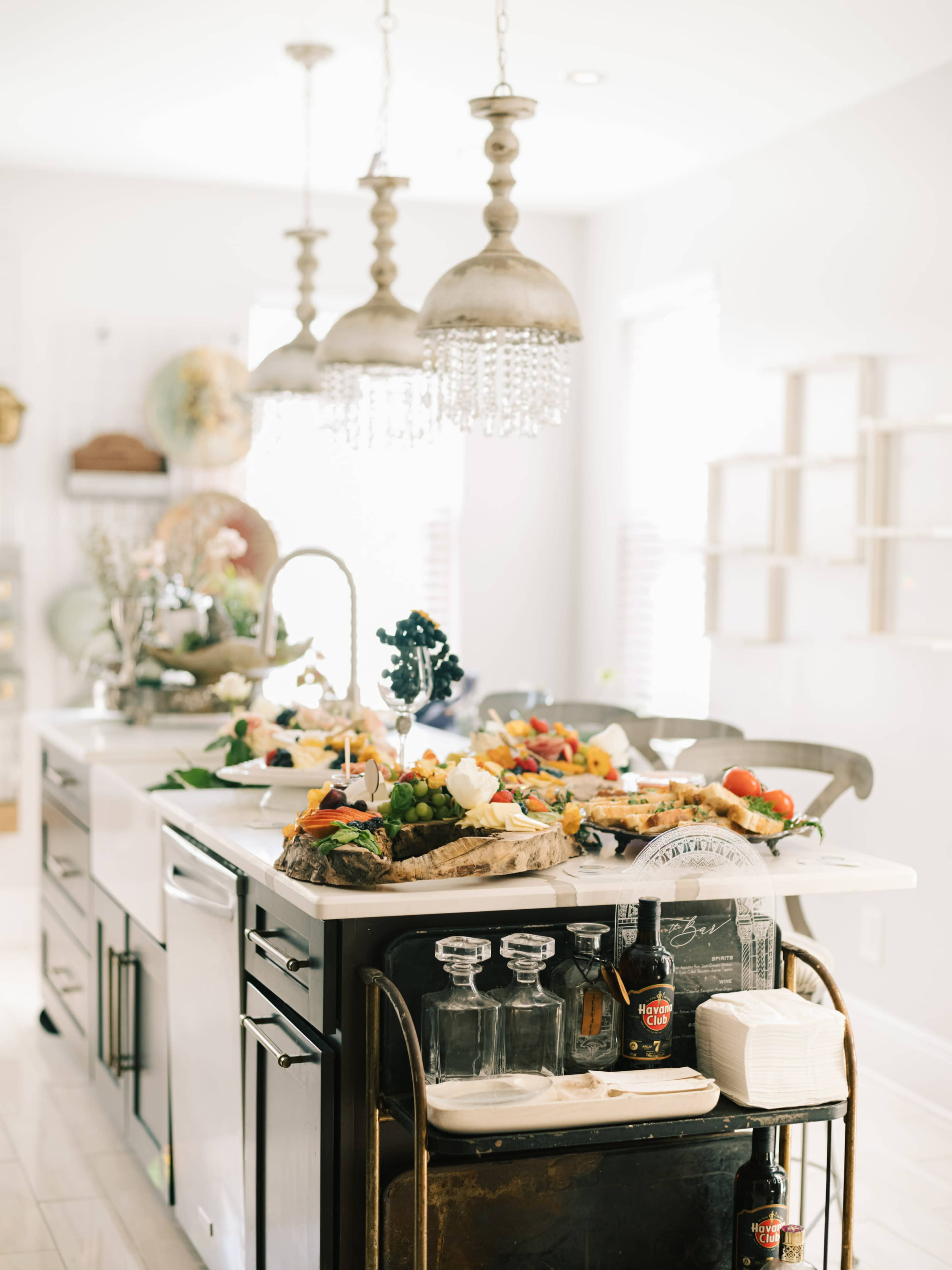 A modern kitchen island displays an array of colorful food items, surrounded by stylish lighting fixtures and equipped with various kitchen tools.