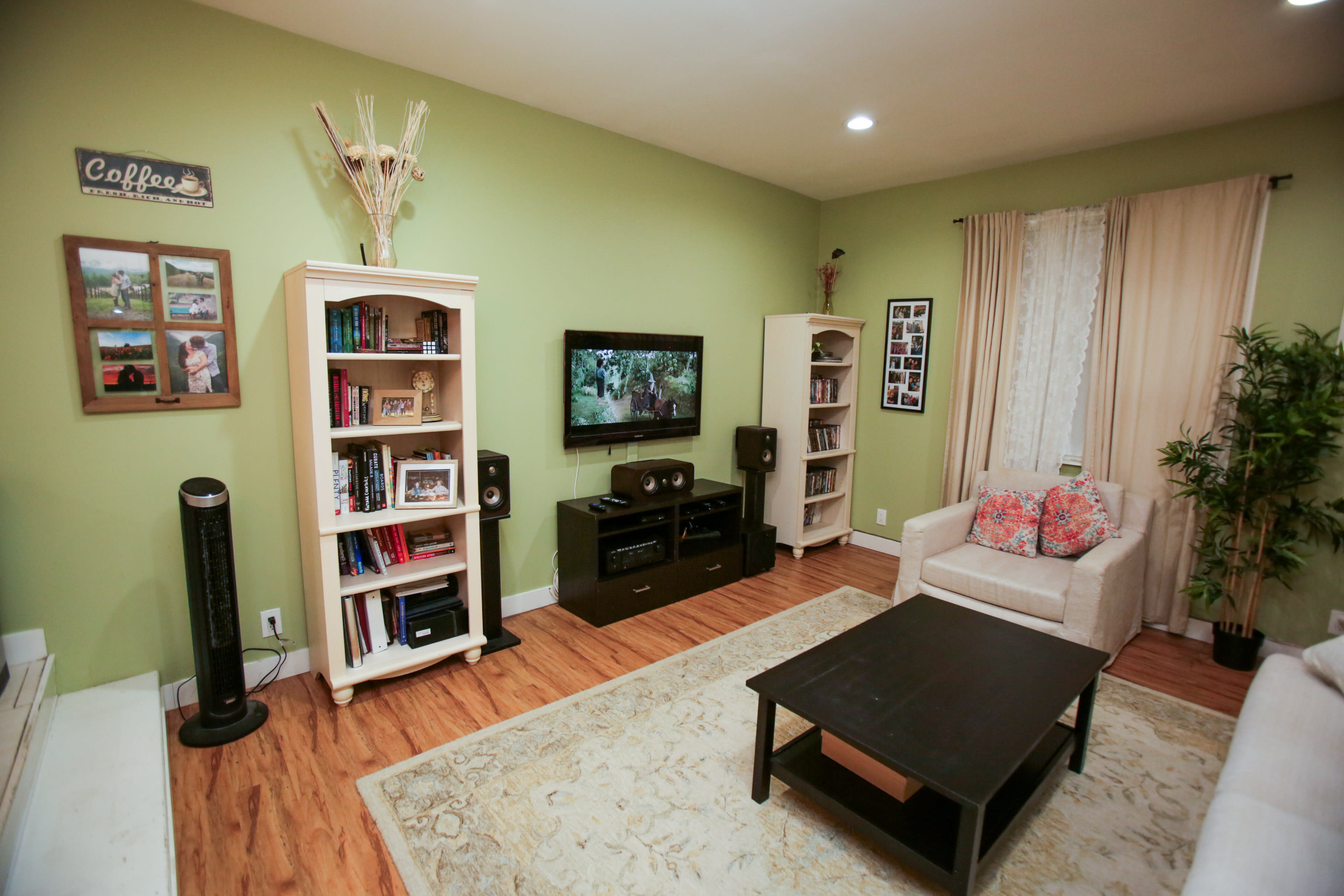 The image shows a cozy living room with a green accent wall, a television on a black media stand, and bookshelves filled with books and framed photos.