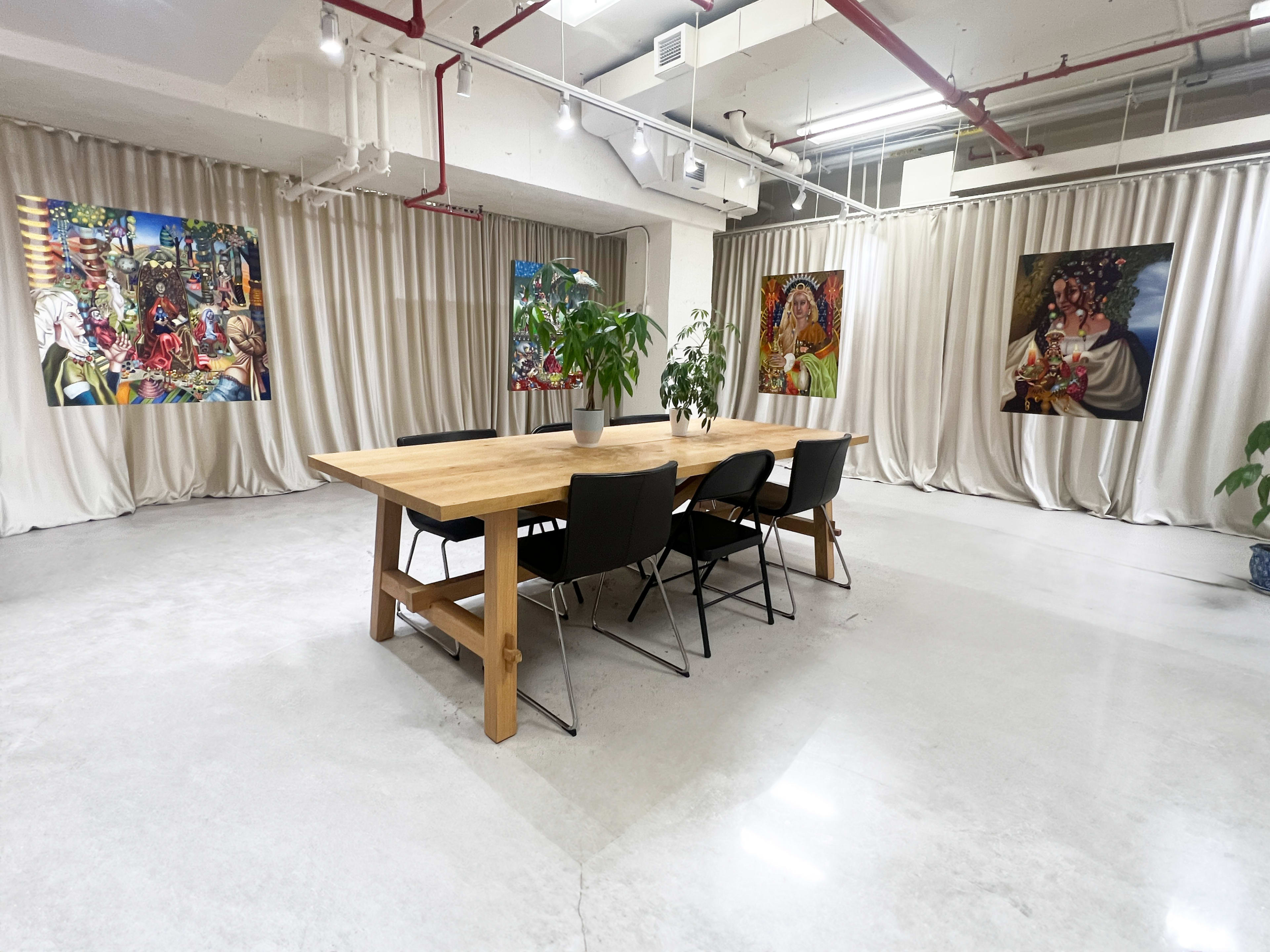 A spacious room with a large wooden table surrounded by black chairs, bordered by walls adorned with colorful artworks and draped curtains.