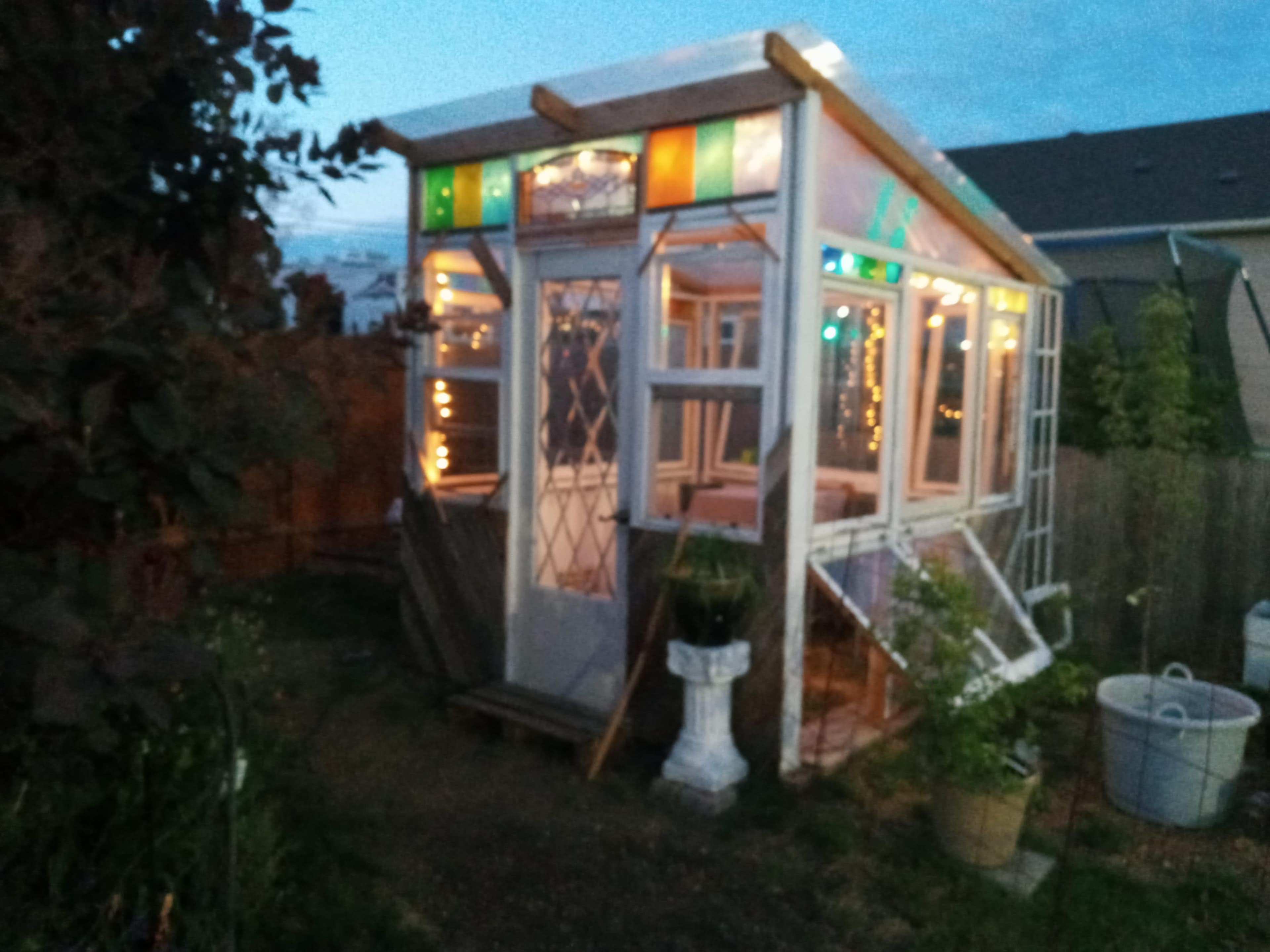 A small garden shed with stained glass windows and decorative lights is set in a backyard.