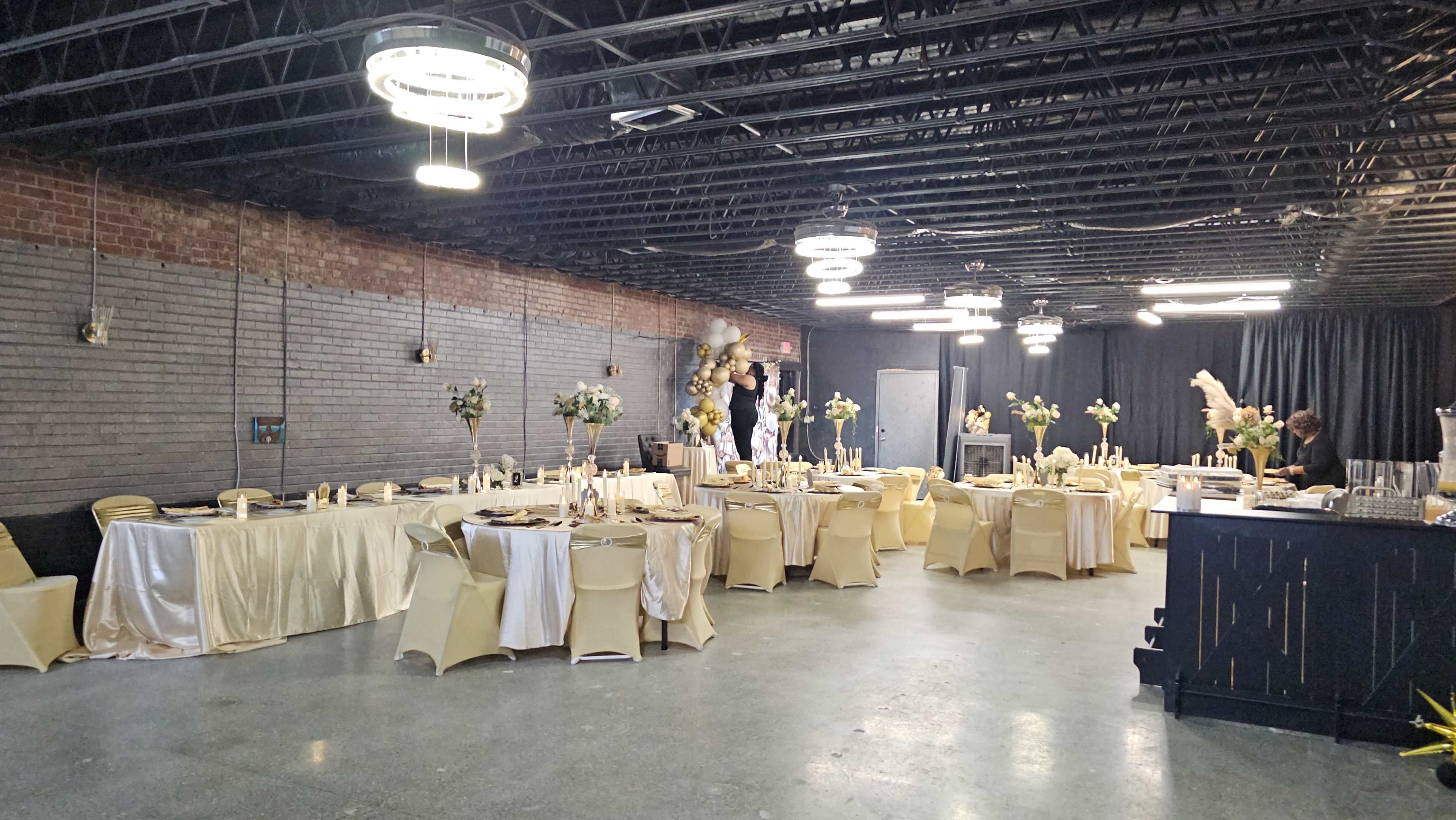 The image shows an elegantly set banquet hall with tables adorned in gold and cream tablecloths and floral centerpieces.