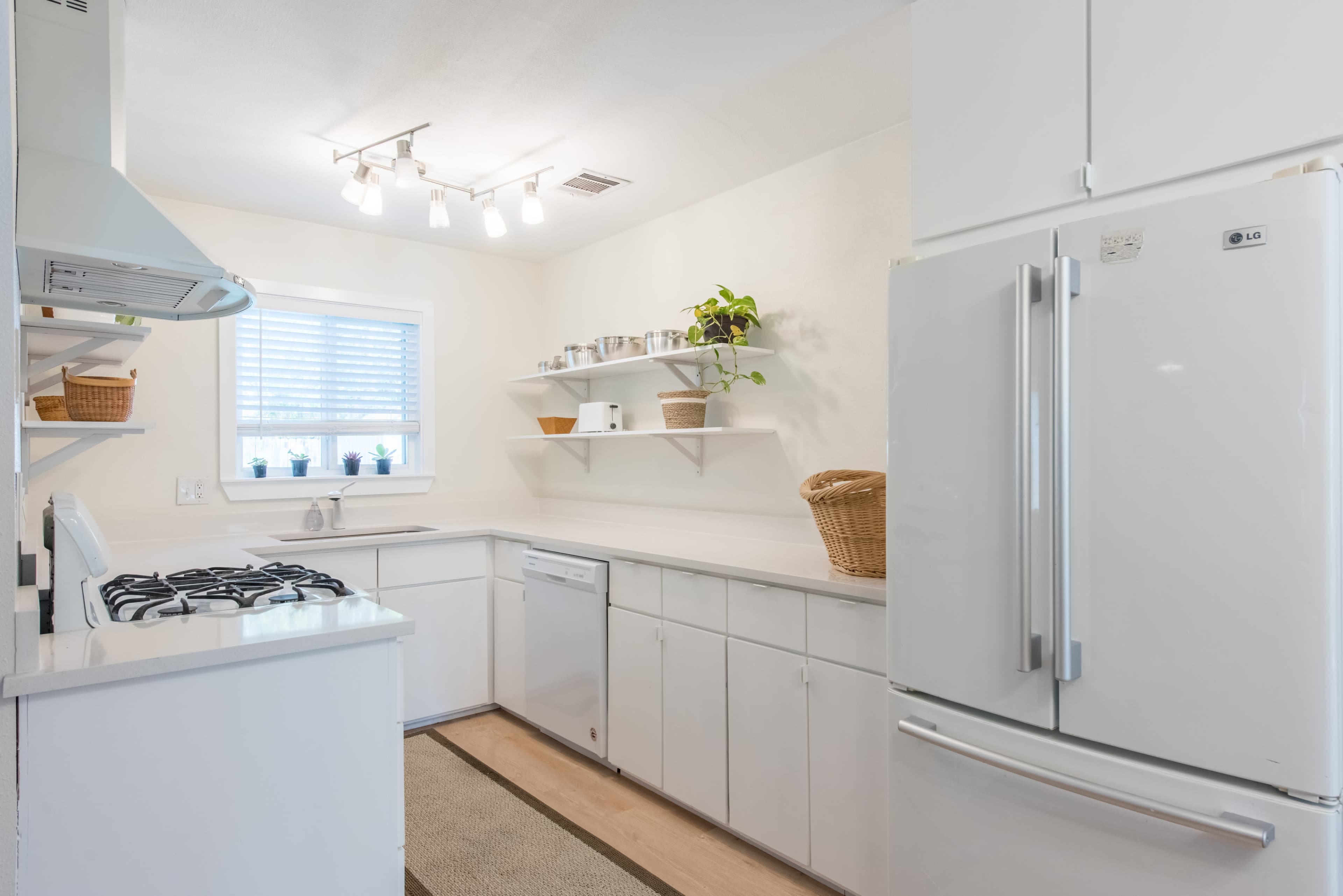 A modern kitchen features white cabinets, a refrigerator, a stove, and open shelving with a few plants and kitchen items.