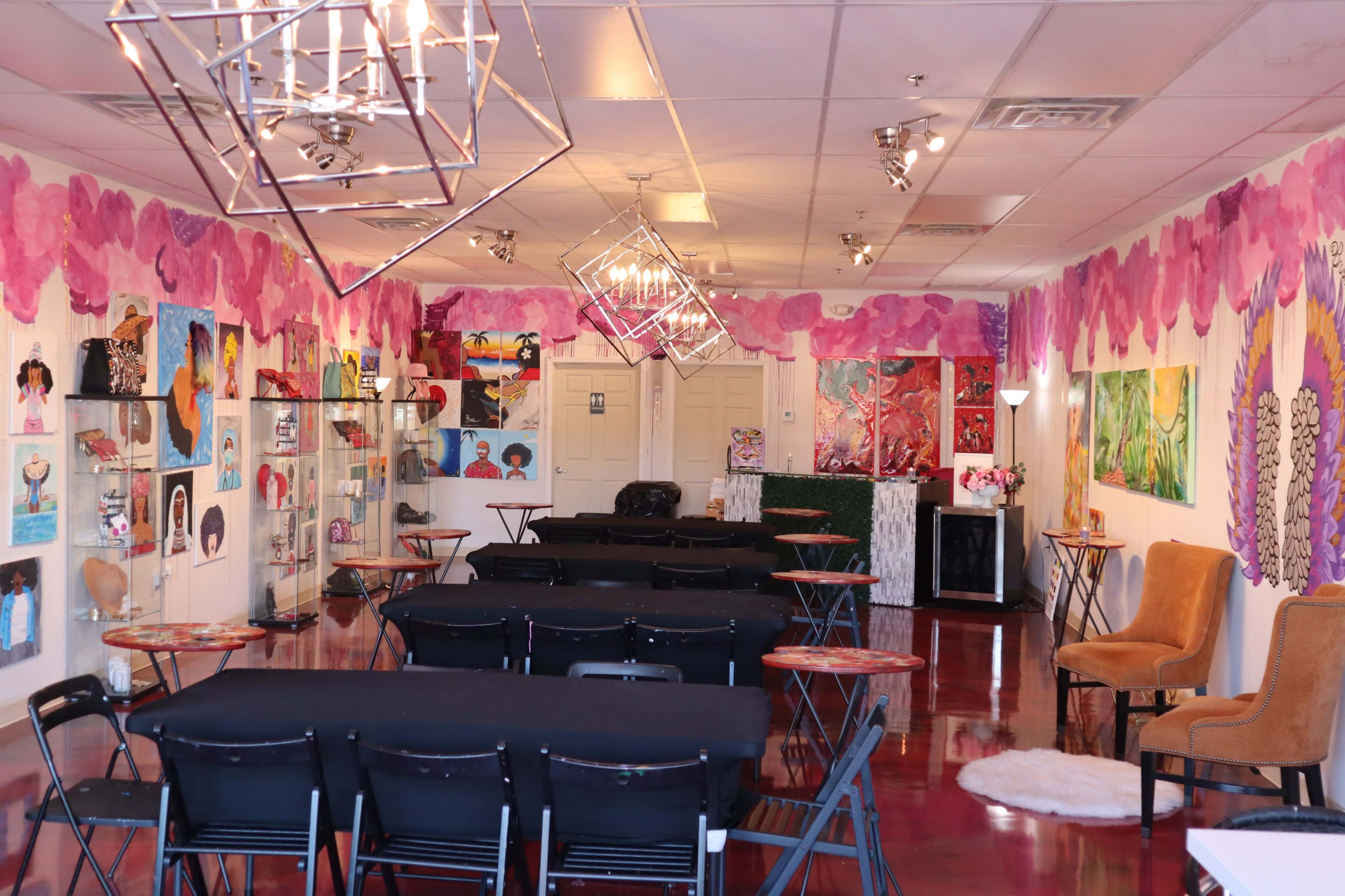 A colorful art studio with tables and chairs arranged for an event, surrounded by vibrant paintings on the walls.