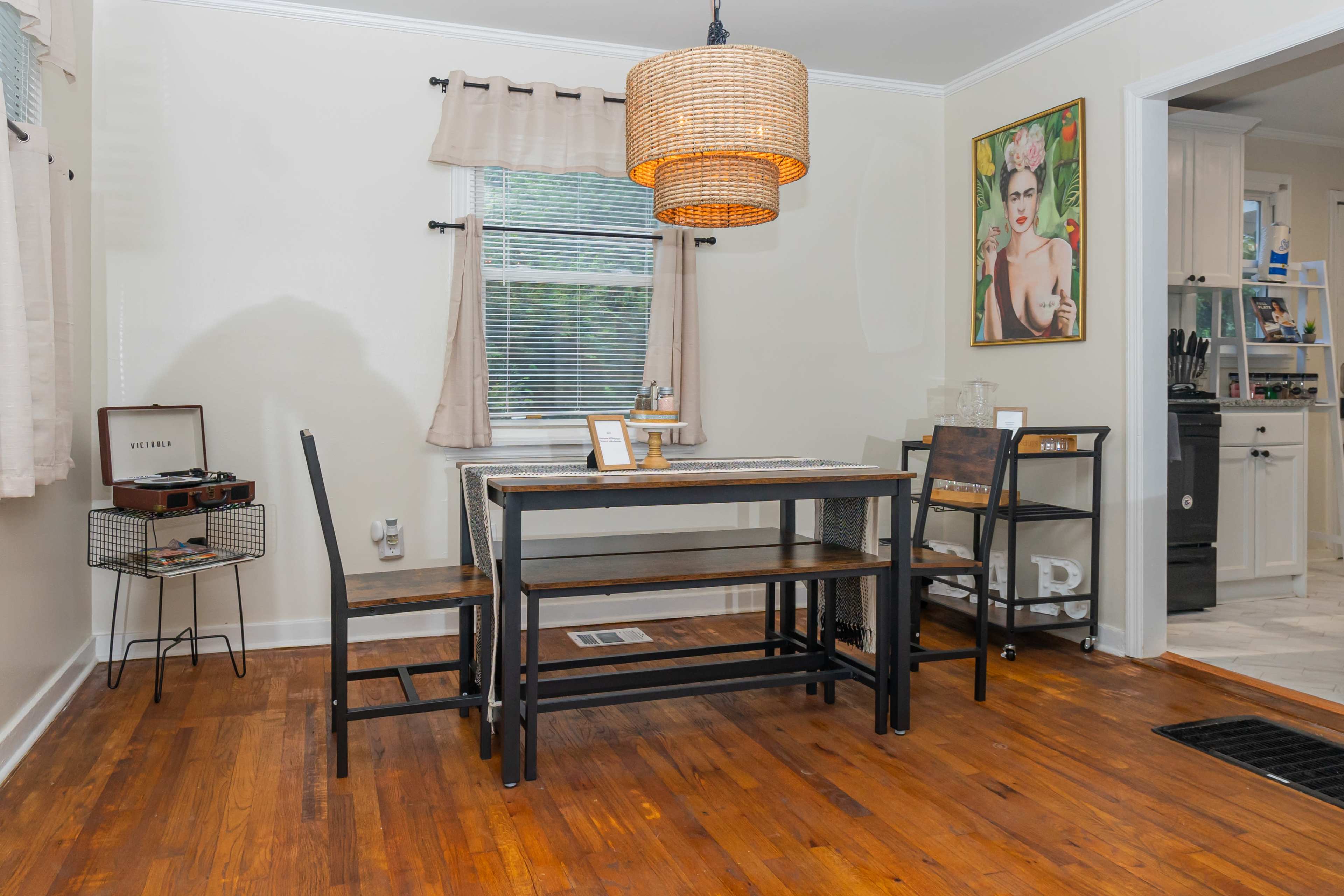 A dining area featuring a wooden table, four chairs, a woven light fixture, and a small side cart against the wall.