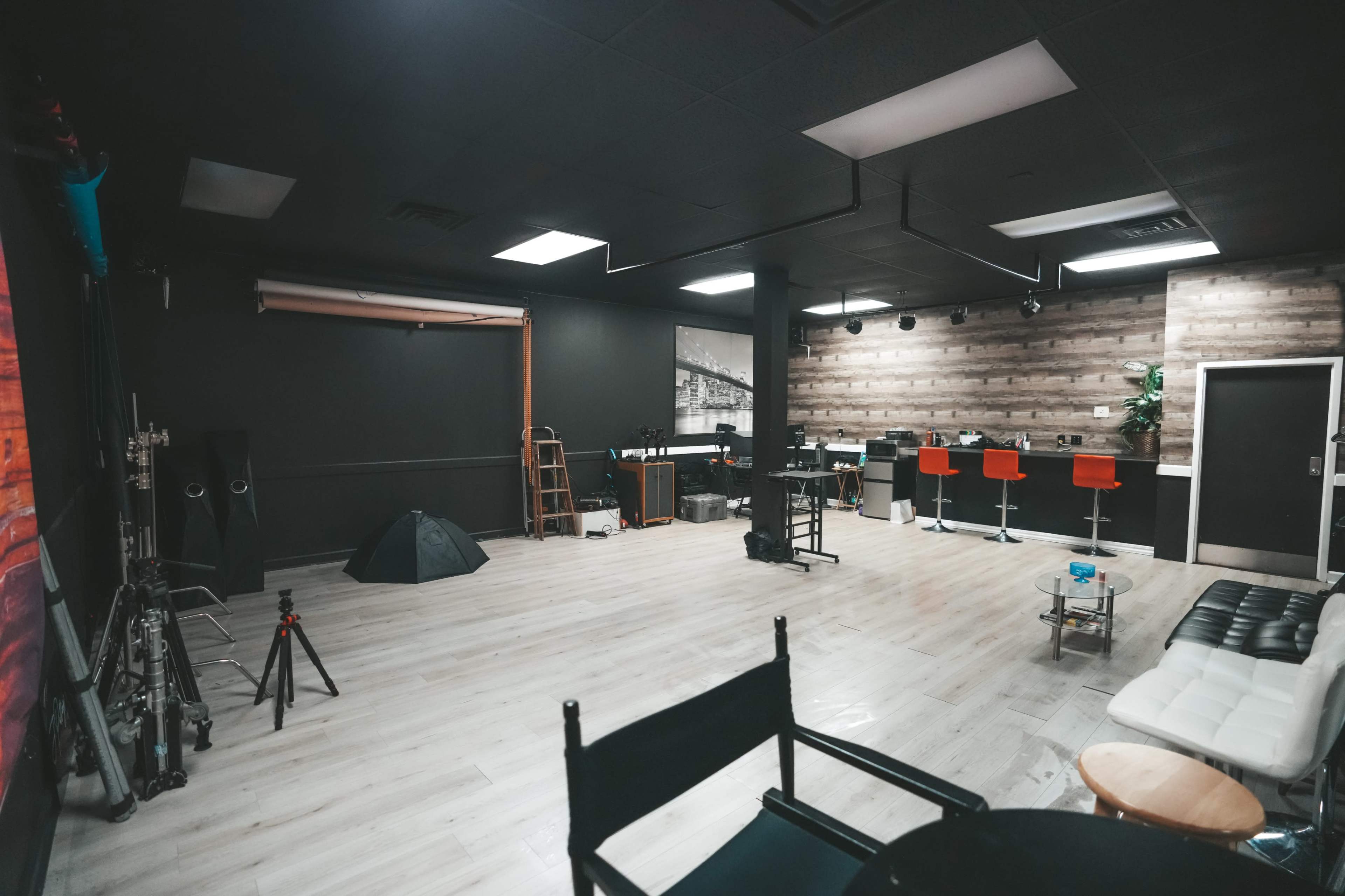 The image shows a spacious studio with a wooden accent wall, a bar area with orange stools, and various photography equipment scattered around.