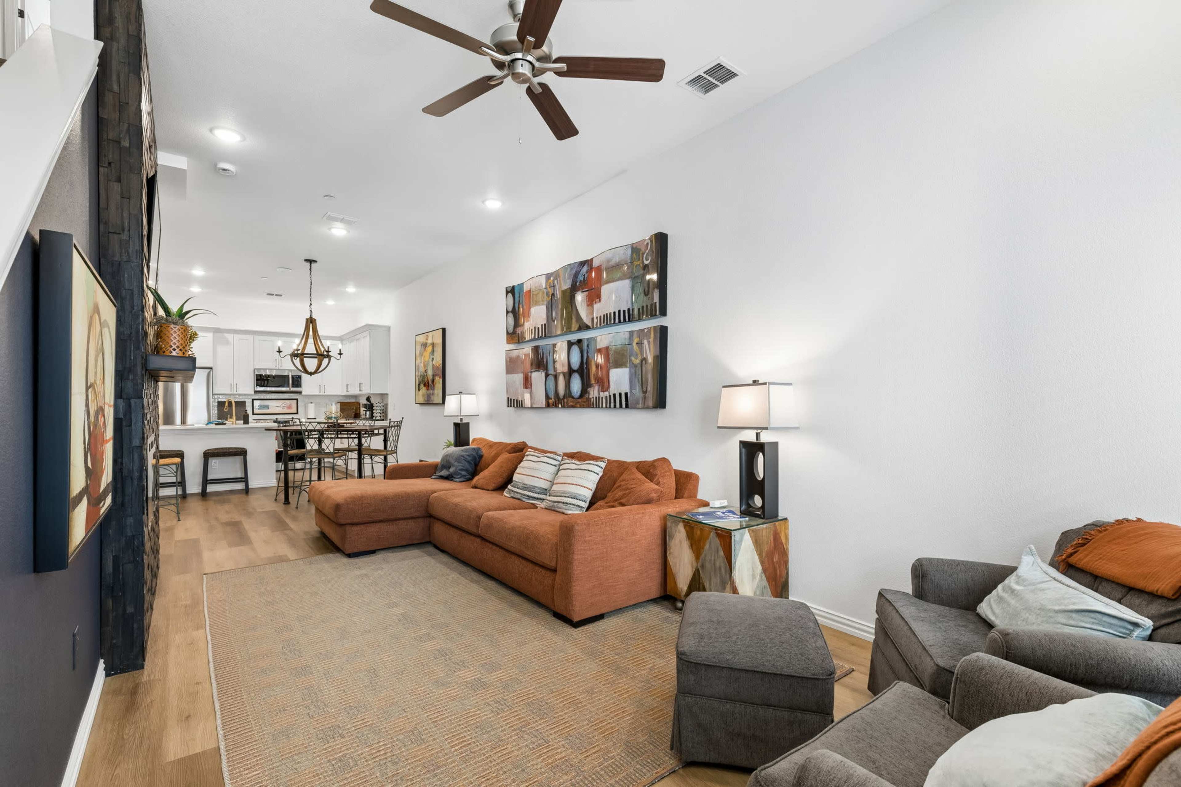 The image shows a modern living room with an L-shaped couch, a couple of armchairs, and an open kitchen area in the background.