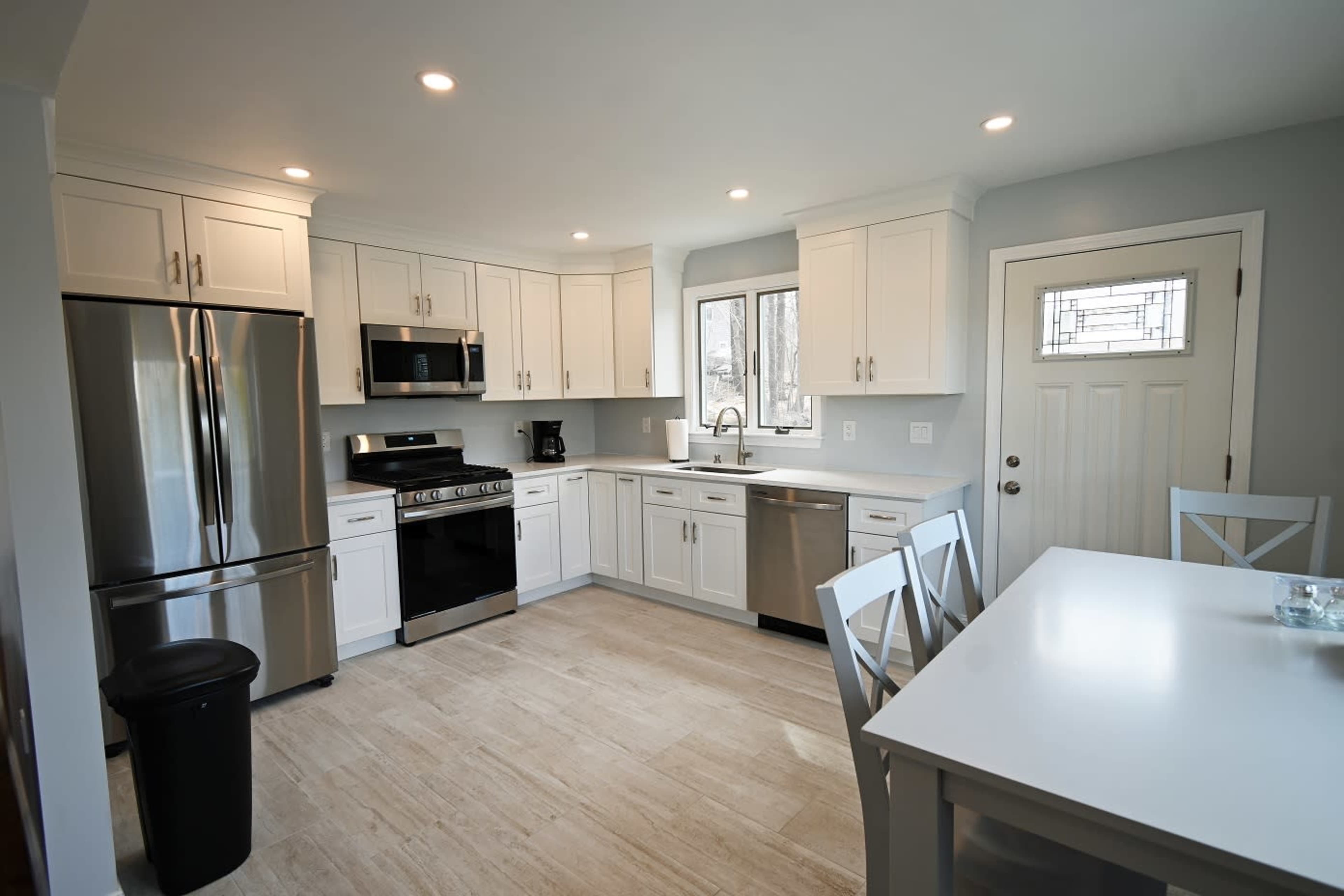 The kitchen features white cabinetry, stainless steel appliances, and a dining table with four chairs.
