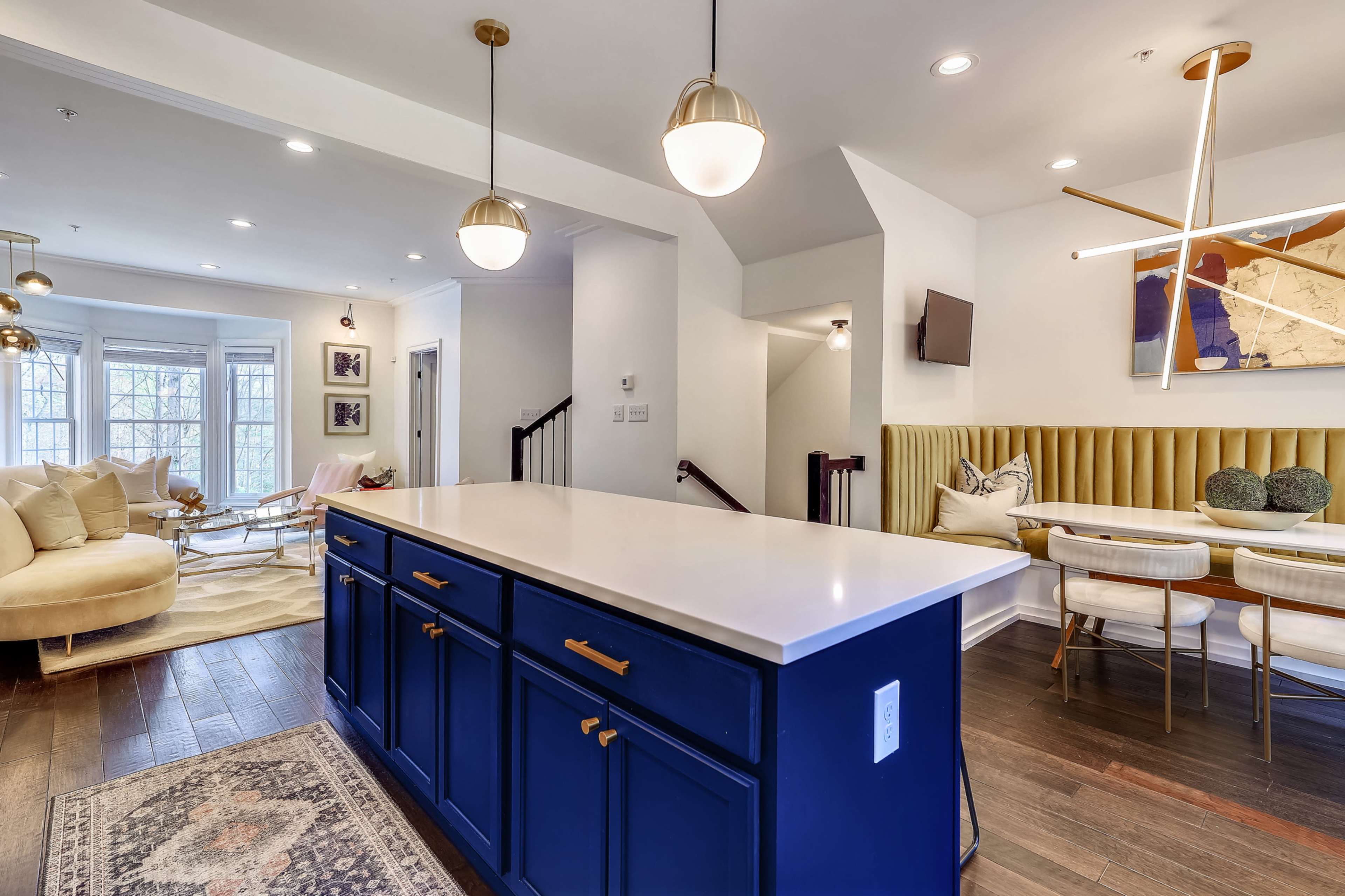 A modern kitchen with a blue island, white countertops, and seating, adjacent to a cozy living area with a light-colored sofa.