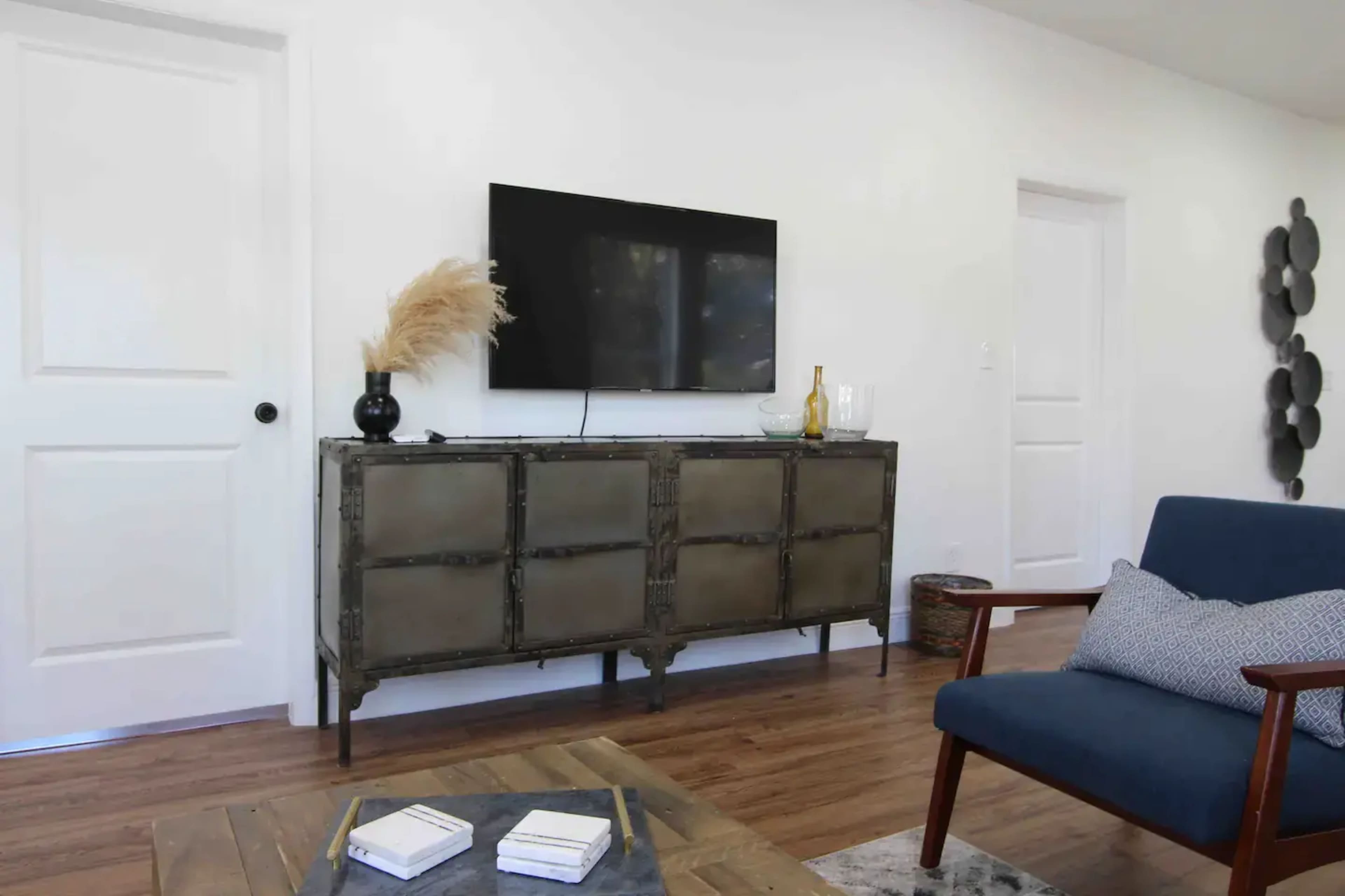 A living room with a wall-mounted TV above a metallic television stand, accompanied by a blue armchair and a wooden coffee table.
