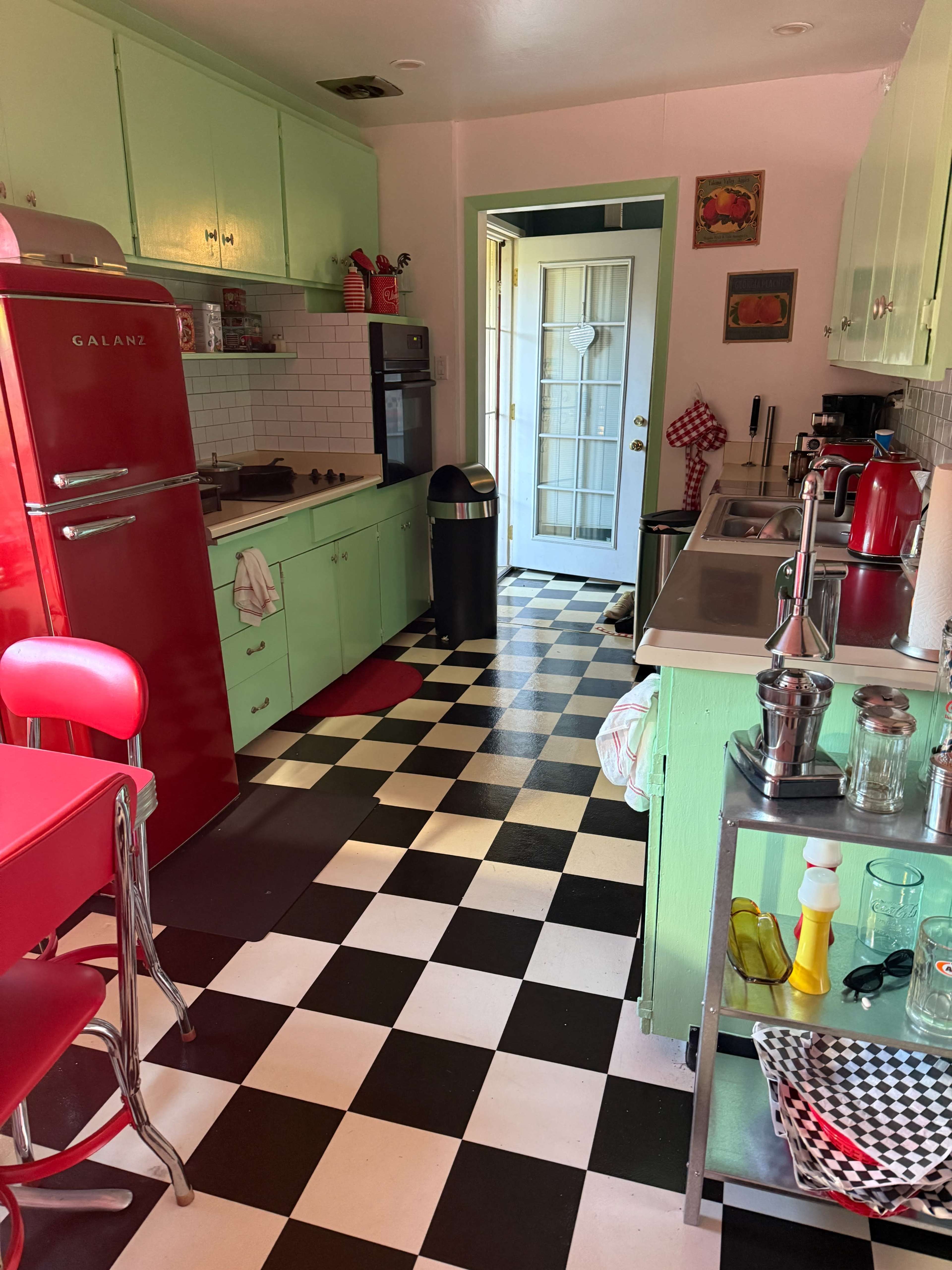 The kitchen features retro-style appliances, including a bright red fridge, green cabinets, and a black and white checkered floor.