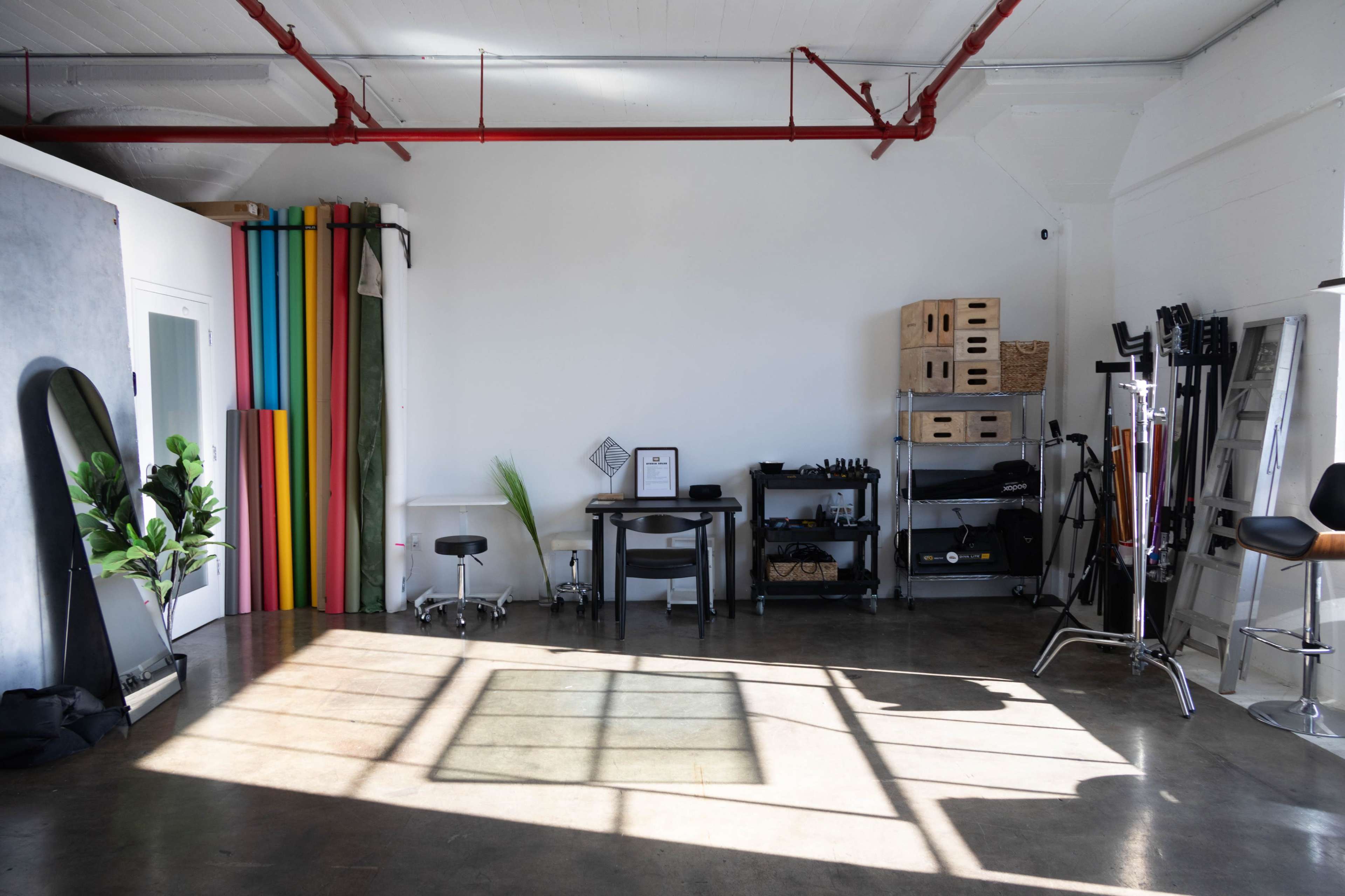 The image shows a spacious, well-lit studio with colorful backdrops, a black table, and various equipment arranged along a wall.