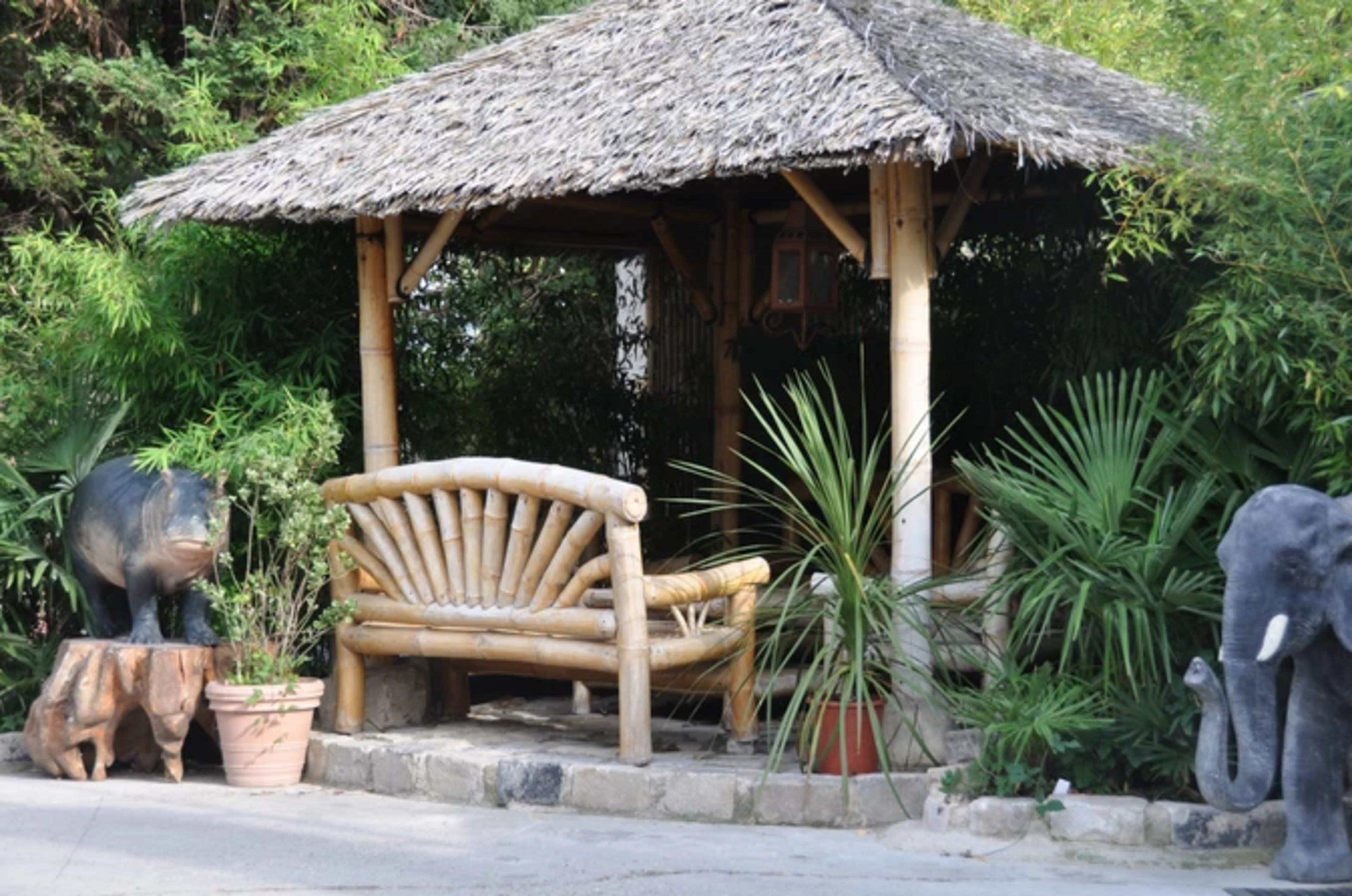The scene features a bamboo gazebo with a rustic bench surrounded by potted plants and animal sculptures, including a pig and an elephant.