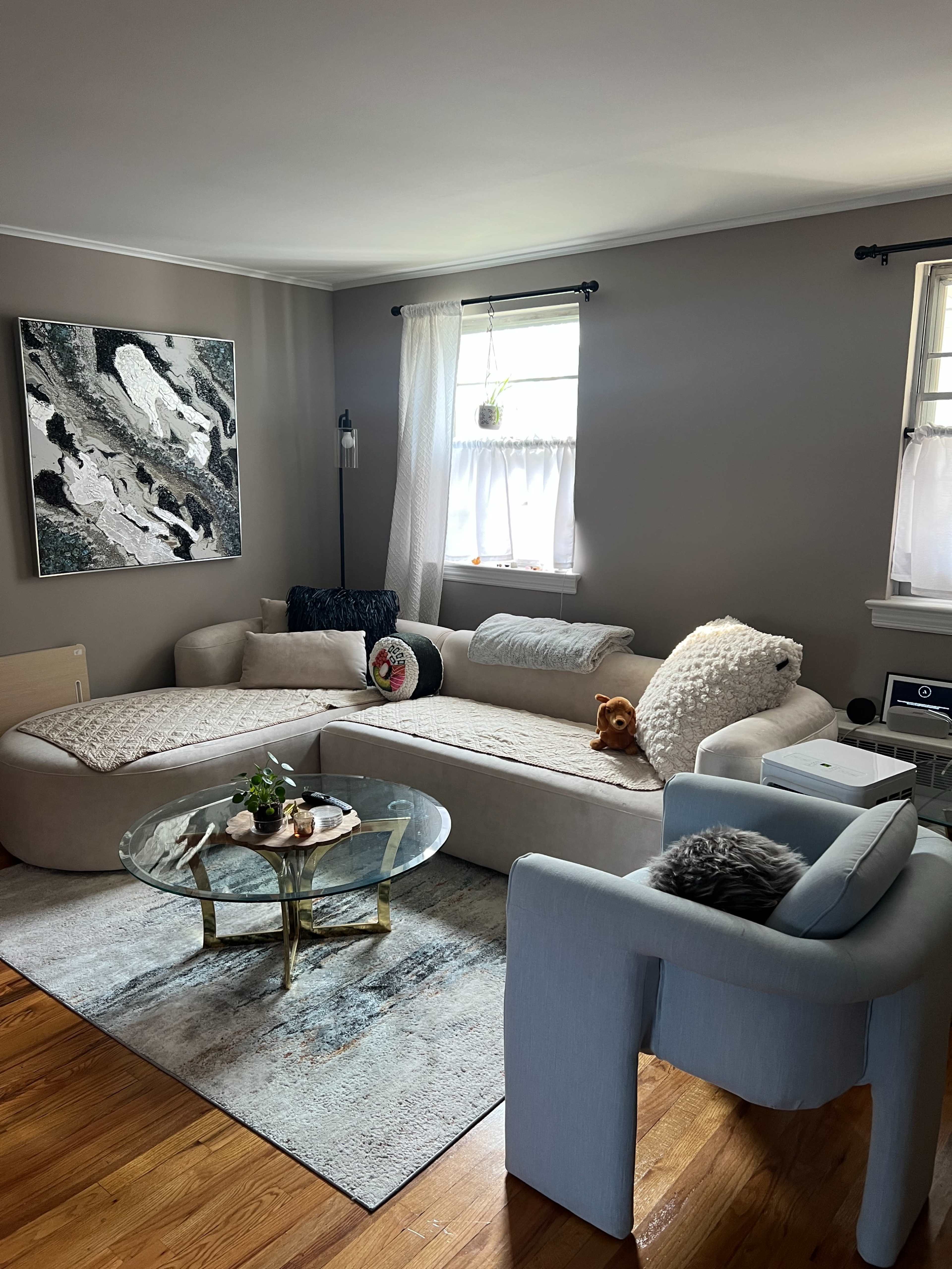 The living room features a large, curved sofa, a glass coffee table, and a decorative rug on hardwood flooring.
