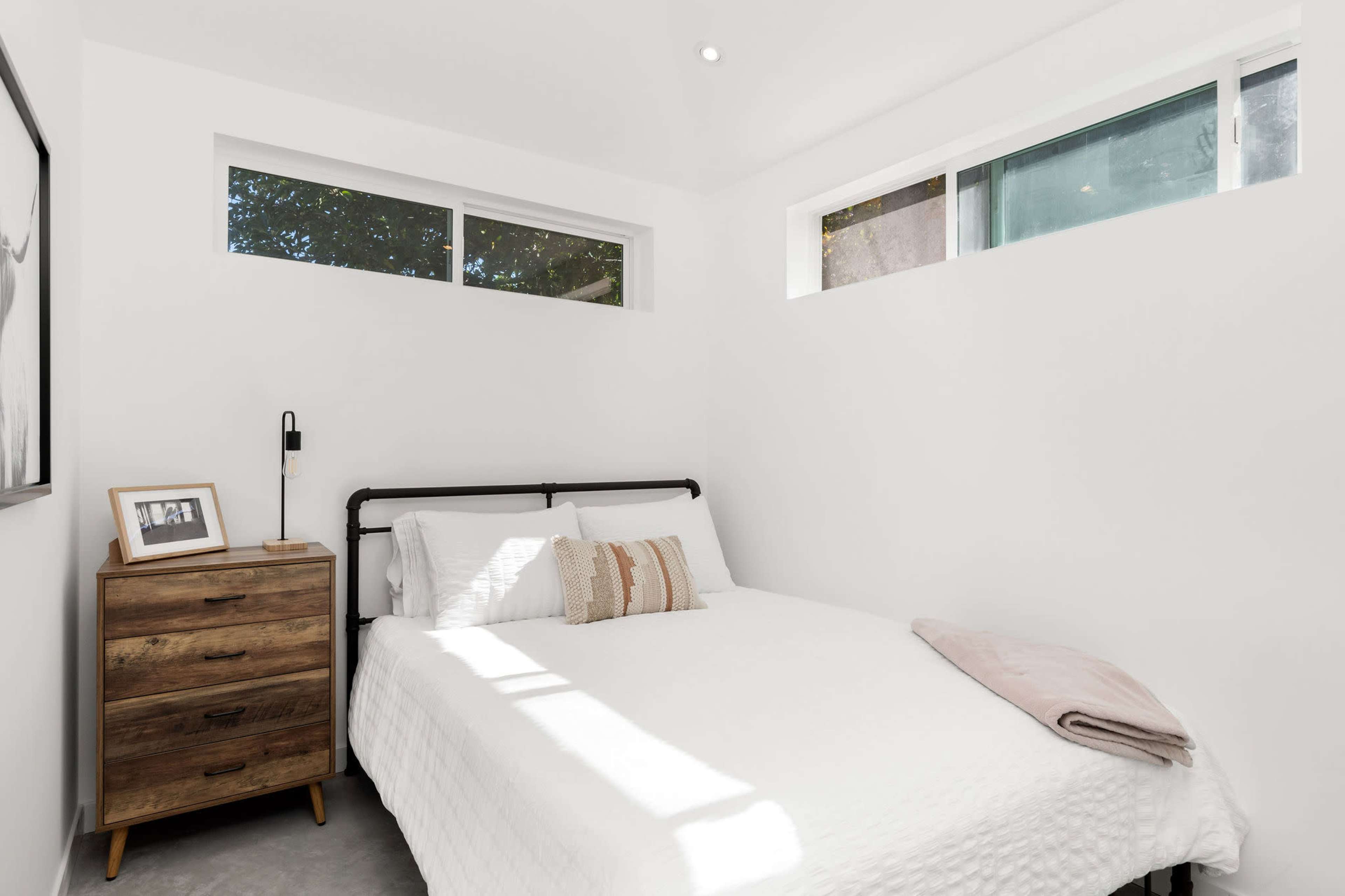 A bright, minimalist bedroom with a bed, a nightstand, and large windows allowing natural light to enter.