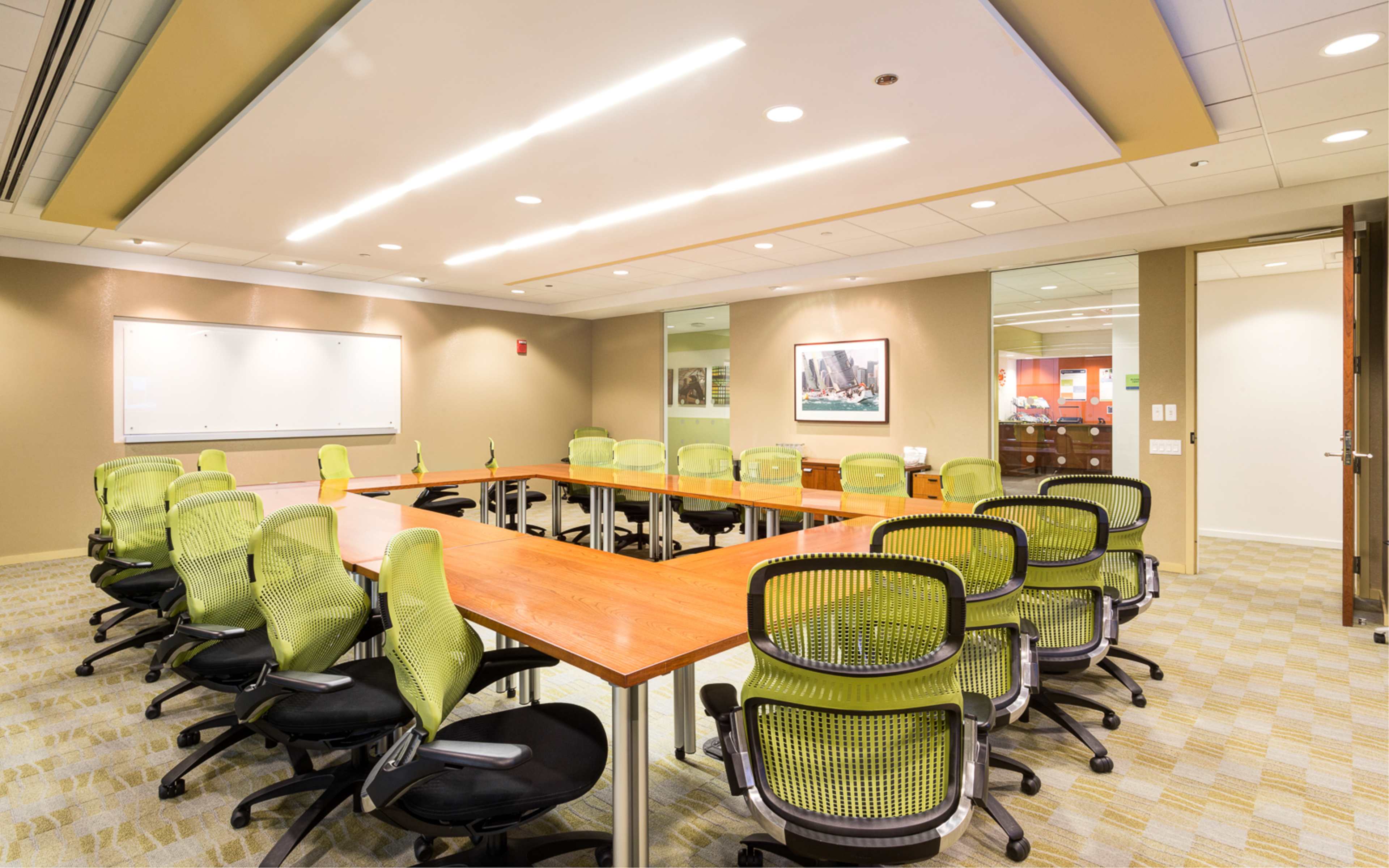 A modern conference room features a large wooden table surrounded by green ergonomic chairs and a whiteboard on one wall.